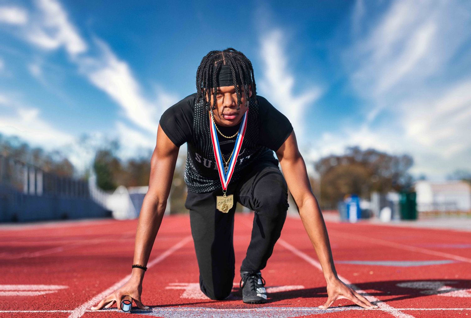 High school senior lifestyle photography session featuring a student in an outdoor setting on a track with a medal around his neck.