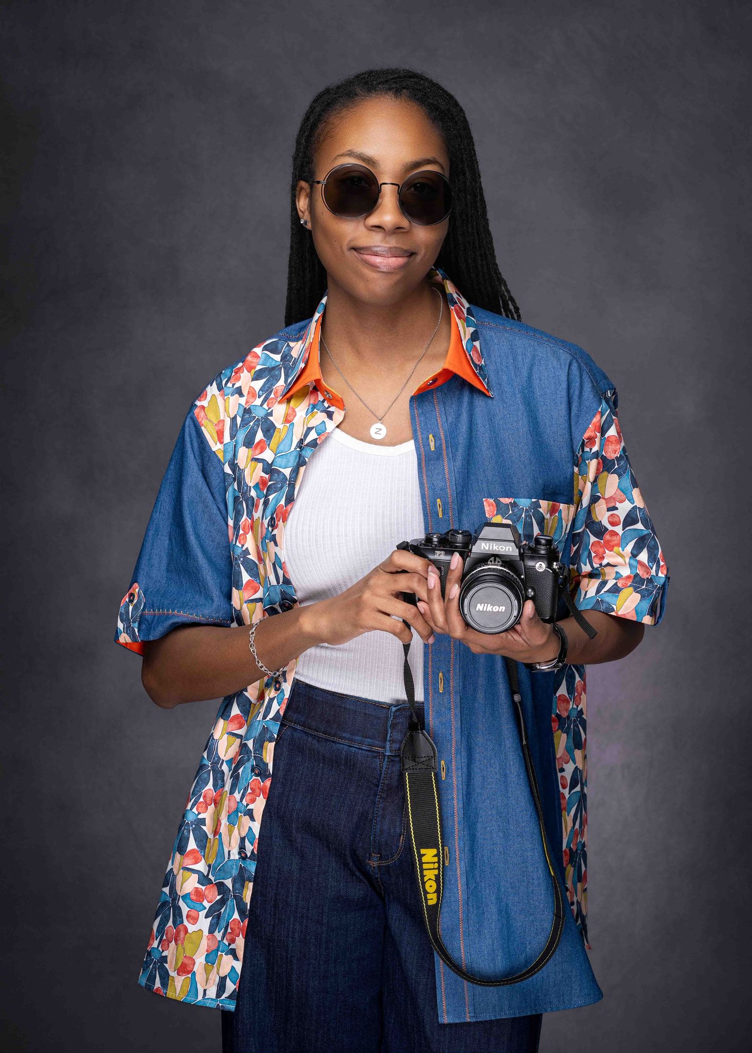 African American female 29th birthday studio photo session; holding a camera wearing sunglasses and a vibrant button down shirt.