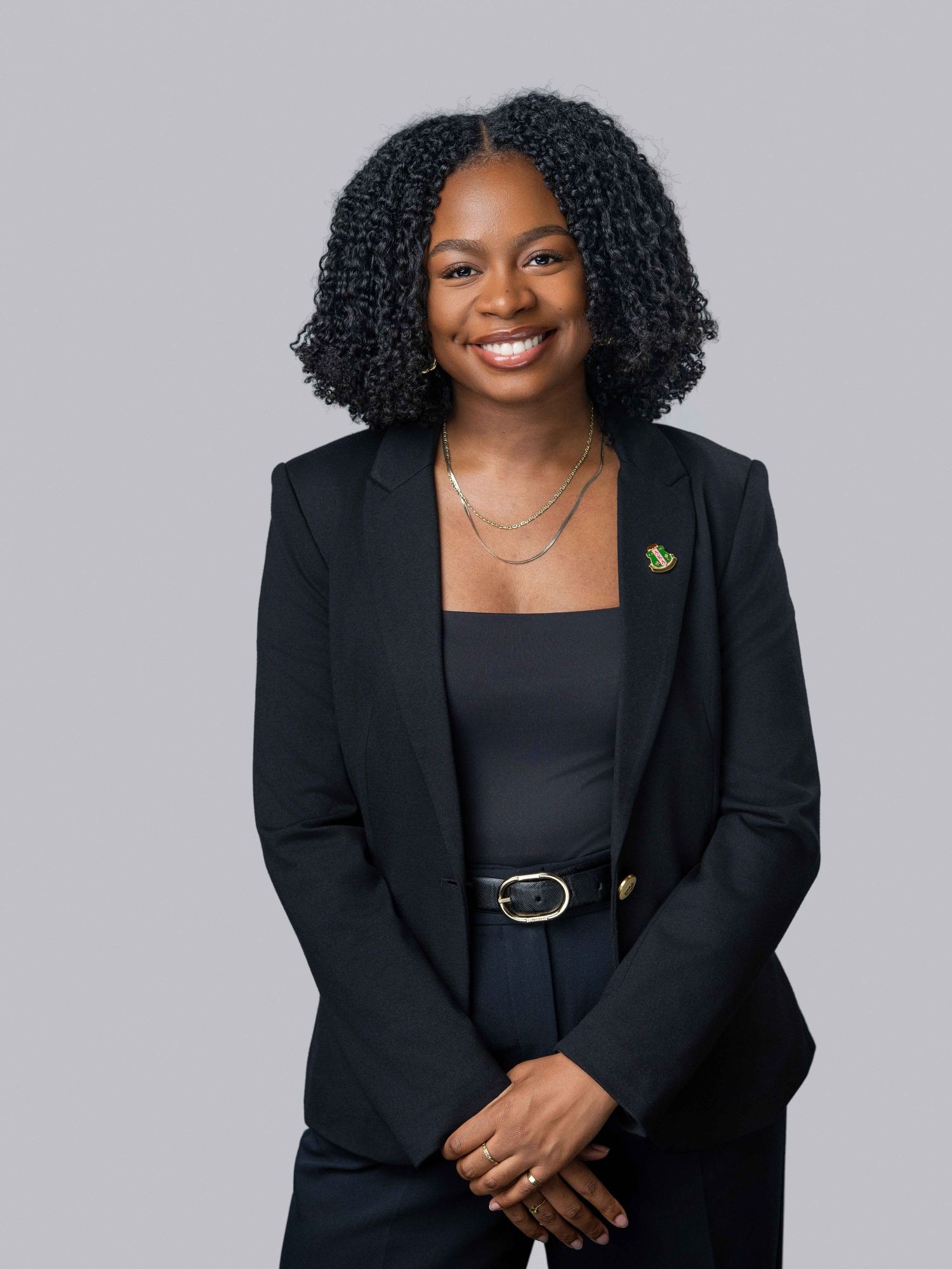 Professional studio portrait of a woman in a black blazer smiling against a neutral gray background.