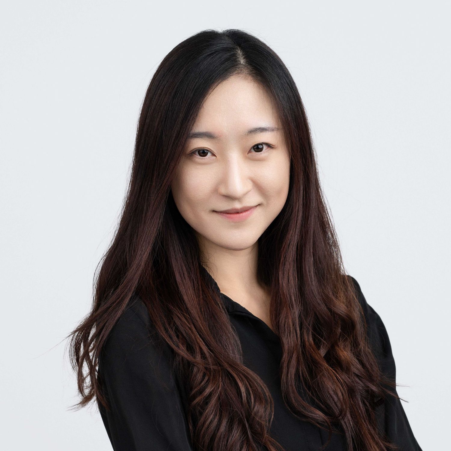 Professional headshot of a woman with long dark hair, wearing a navy blue blazer against a light gray background.