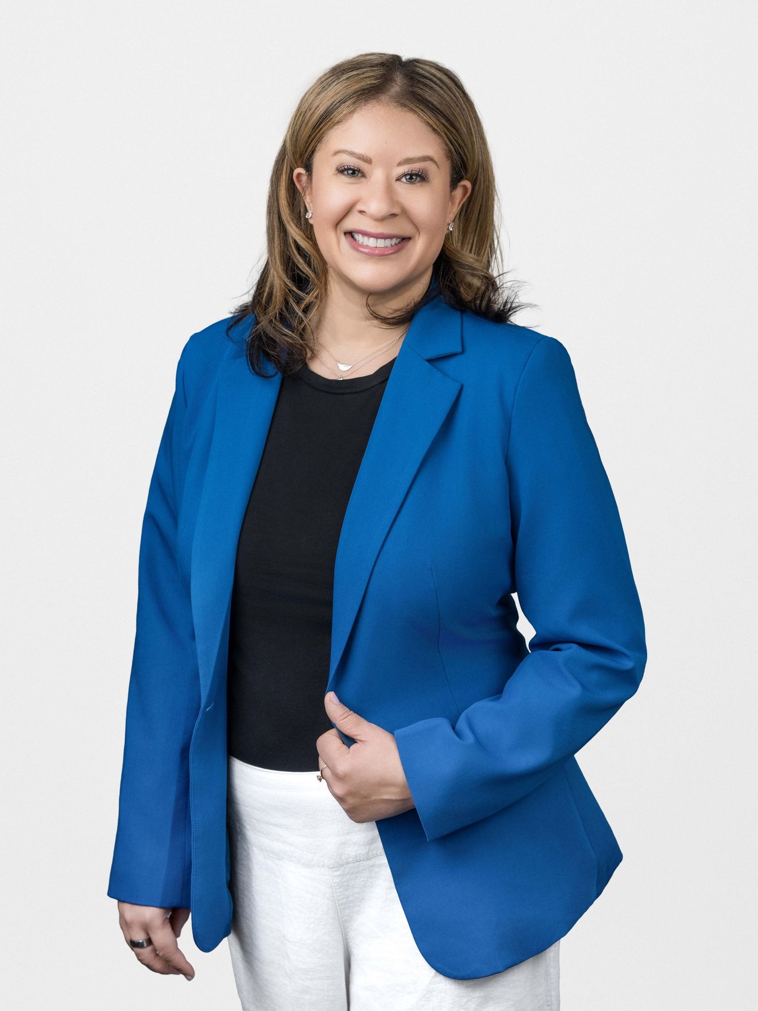 Professional studio headshot of a smiling woman wearing a blue blazer and white top against a neutral gray background.
