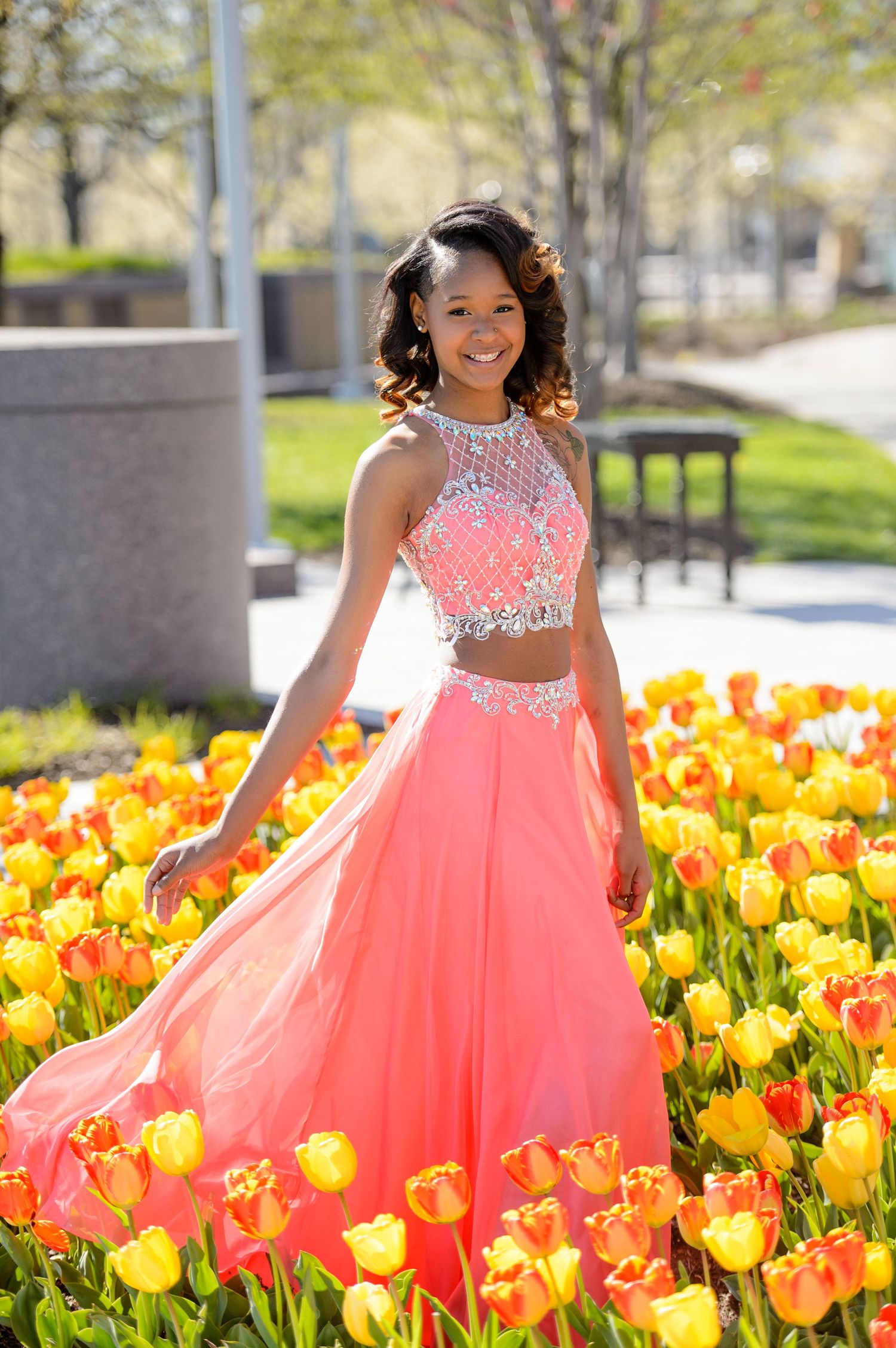 Creative outdoor portrait of a high school senior standing in a bed of colorful tulips wearing a pink prom dress.