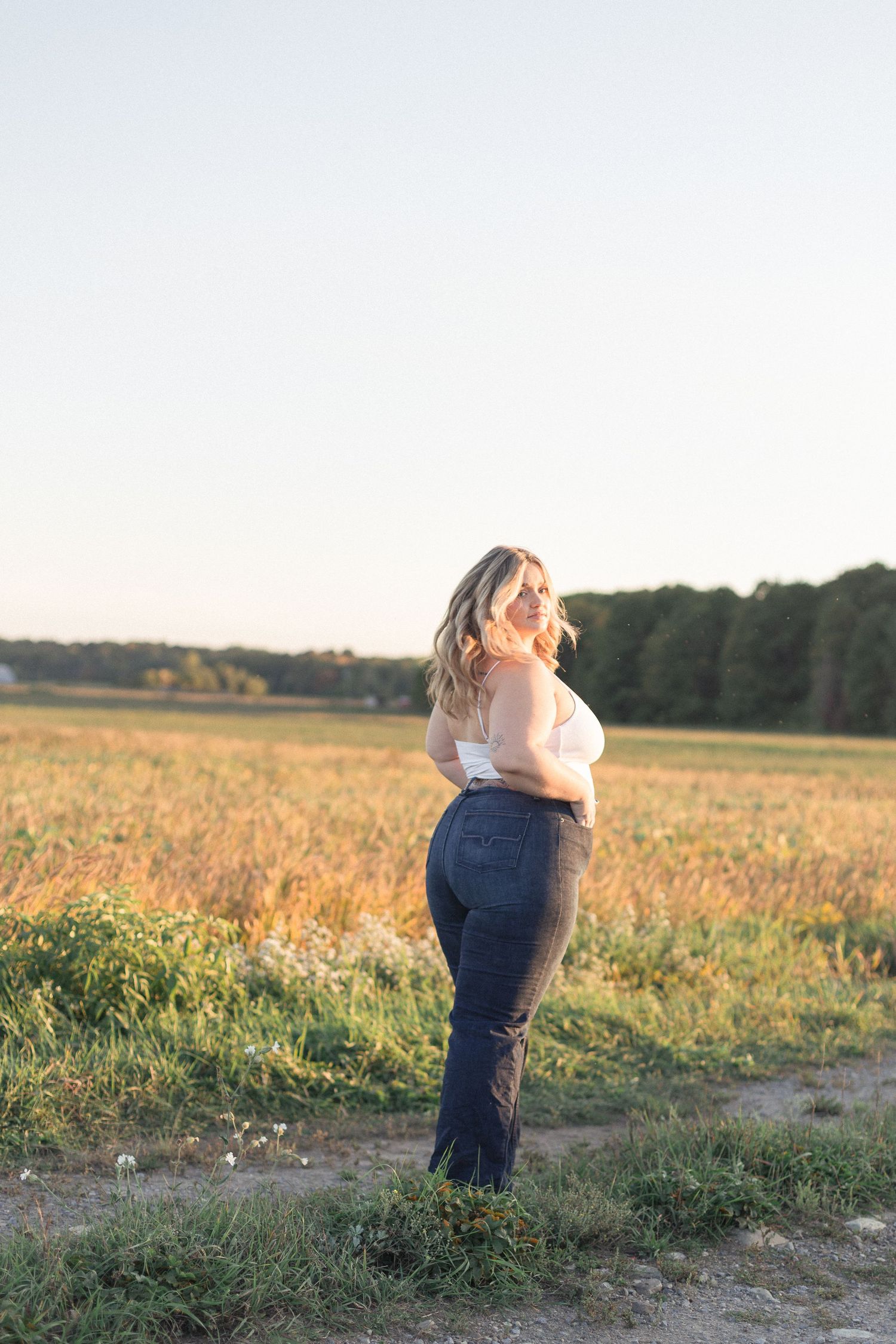 Femme photographiée de profil dans un champ, éclairée par la lumière chaude du coucher du soleil.