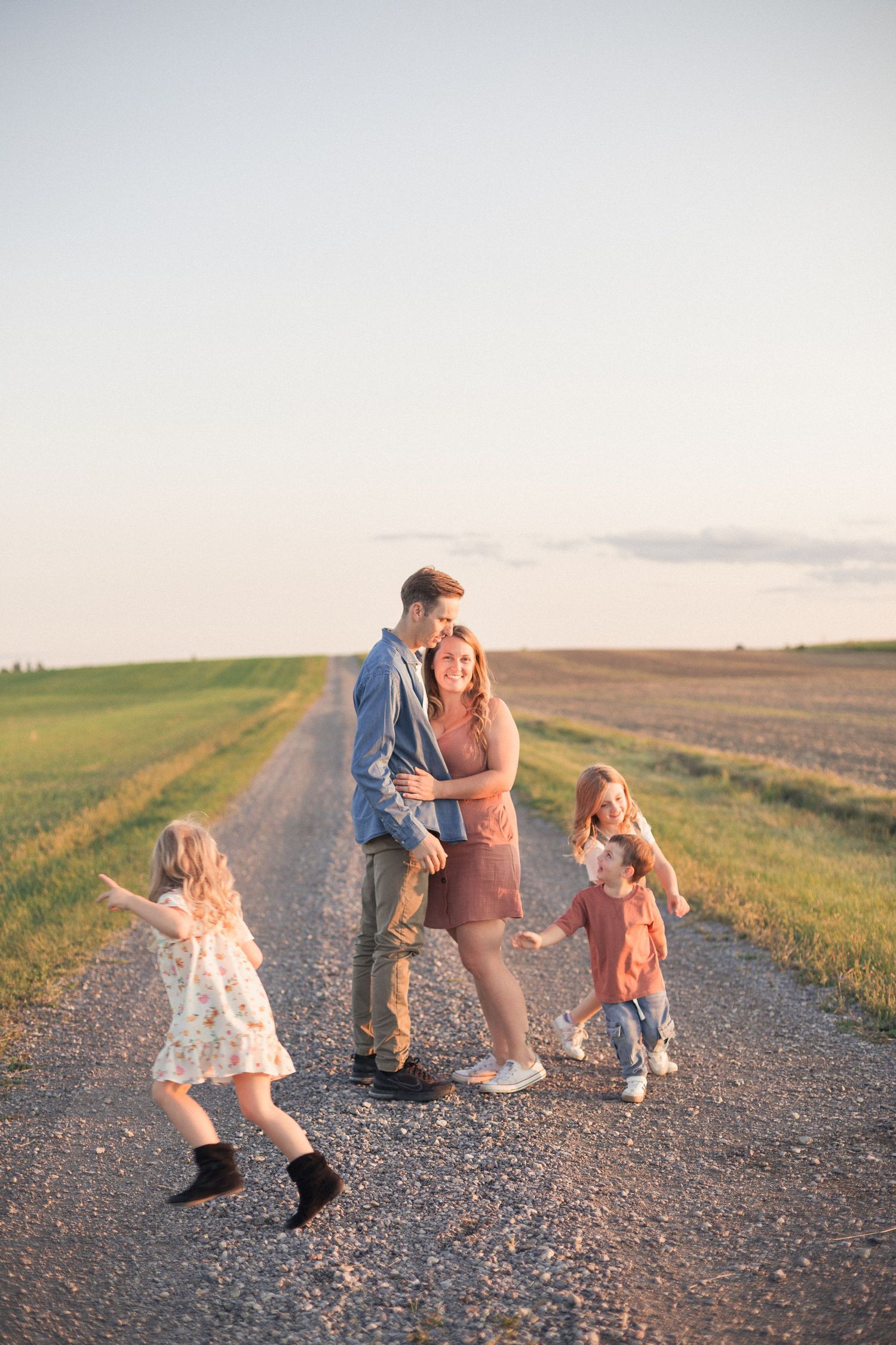 Des enfants qui cours autour de leur parents qui s'enlacent debout sur une route de terre.