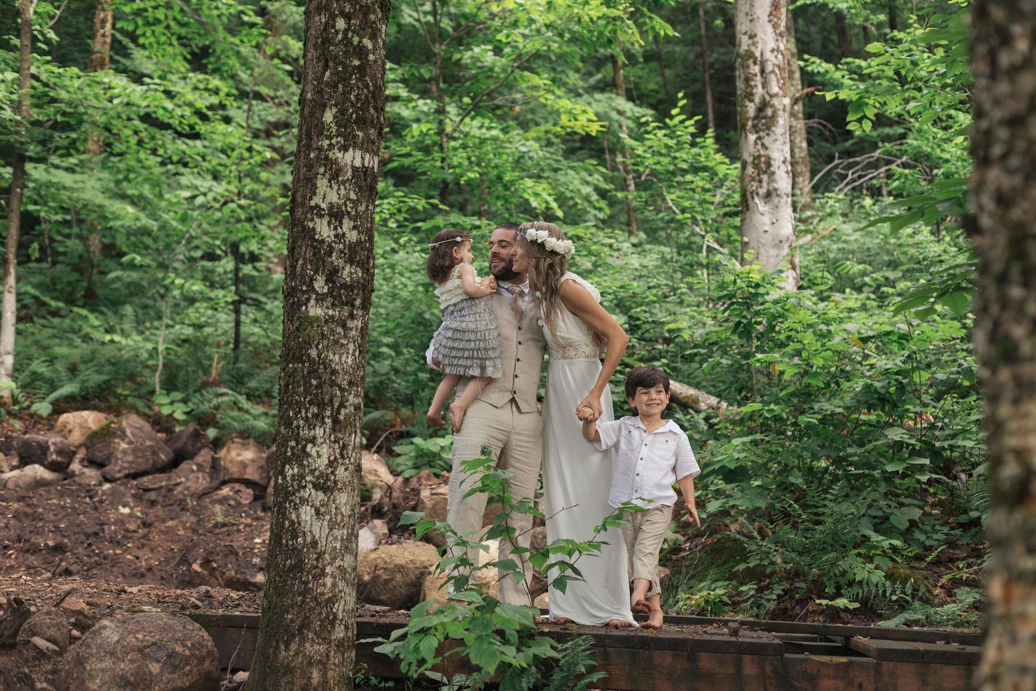 Une famille marchant pieds nus dans la forêt, sur un pont de bois.