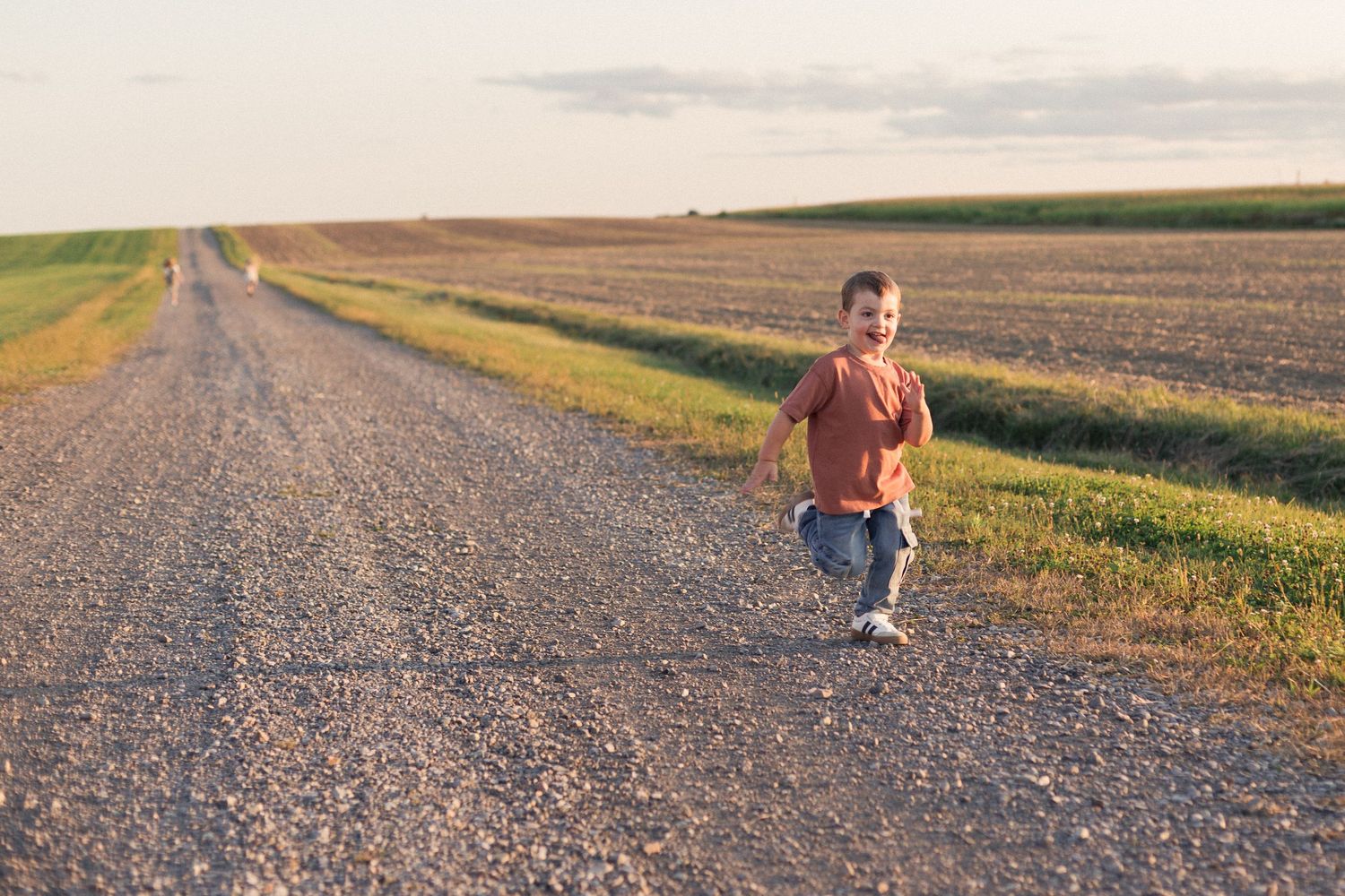 Un enfant qui court sur une route de terre entourée de champs