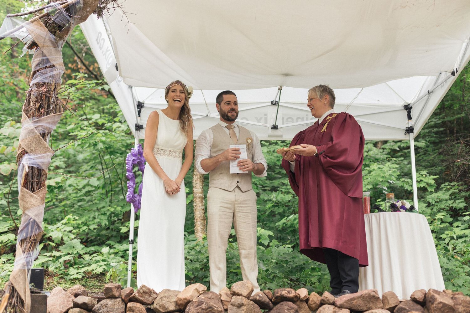 La mariée qui éclate de rire devant les invités et le célébrant, dans un décor naturel.
