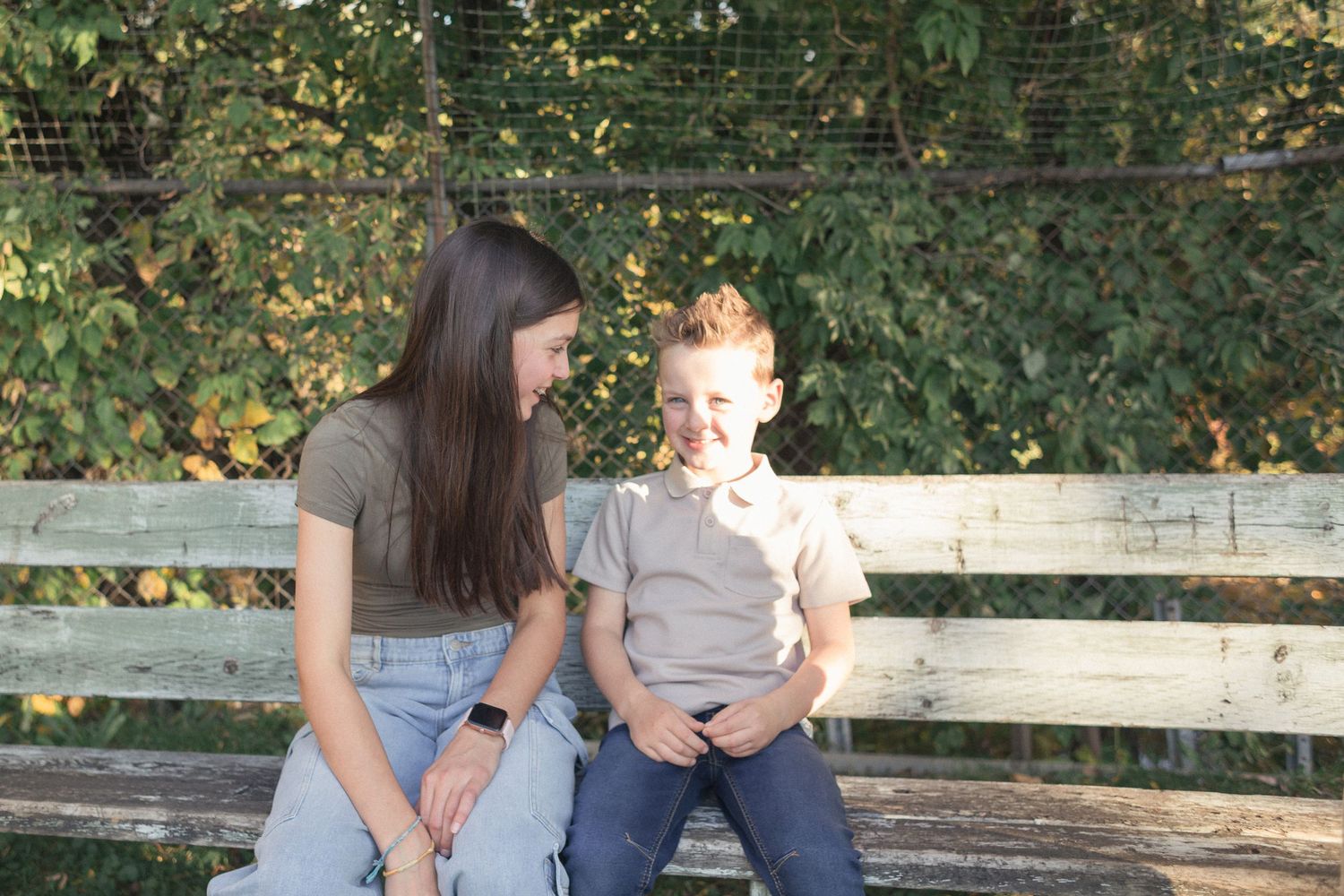 Un enfant et sa grande soeur lui souriant, assis sur un vieux banc de bois.