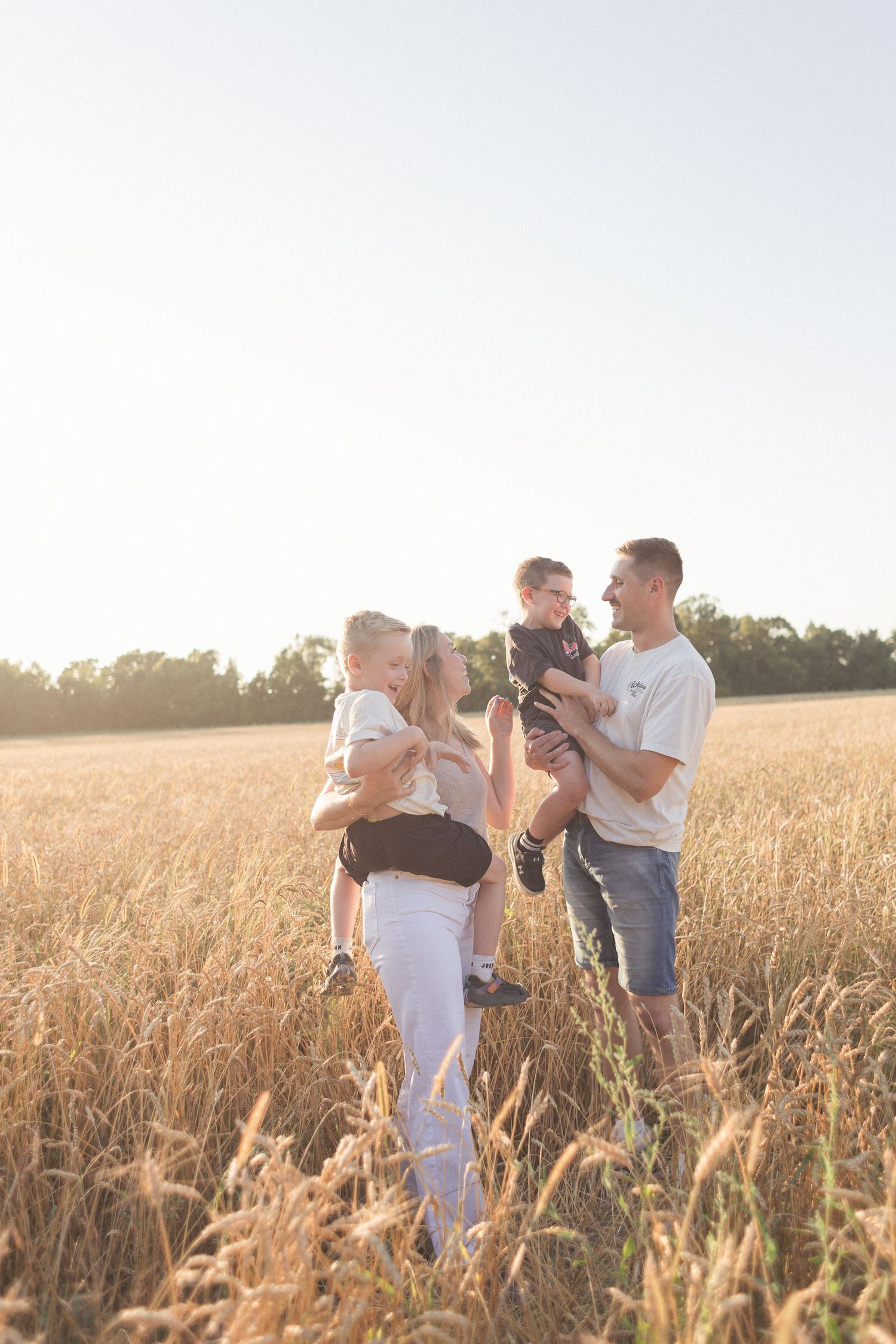 Séance photo de famille dans un champ de blé à la fin de l'été en lumière naturelle.