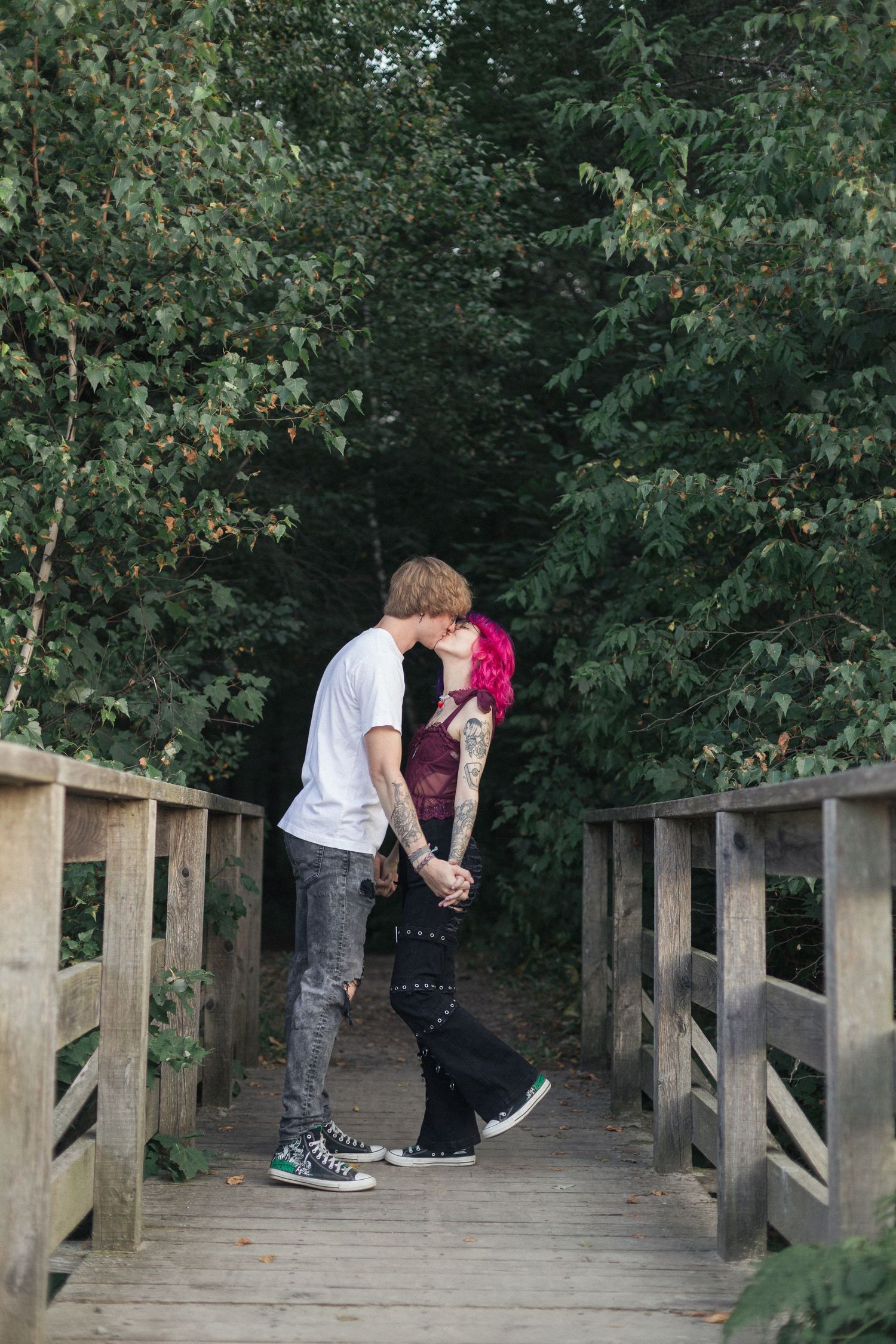 Un couple partageant un tendre baiser sur un pont en forêt.