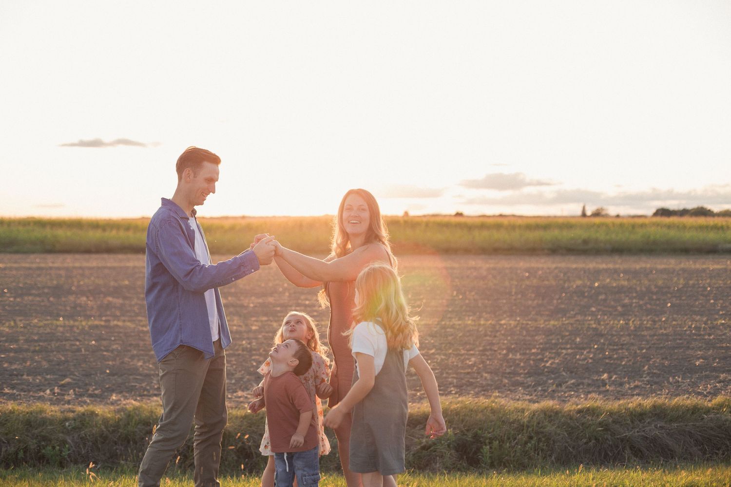 Un couple et leurs enfants qui dansent ensemble dans un champs au coucher du soleil
