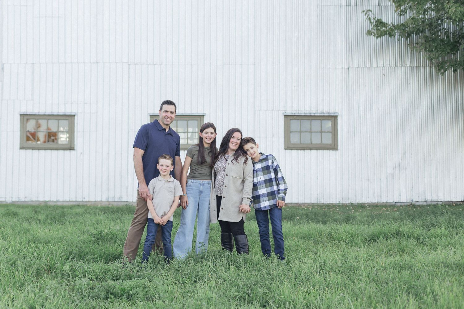 Une famille posant pour un portrait sur un terrain vague devant un mur de garage blanc.