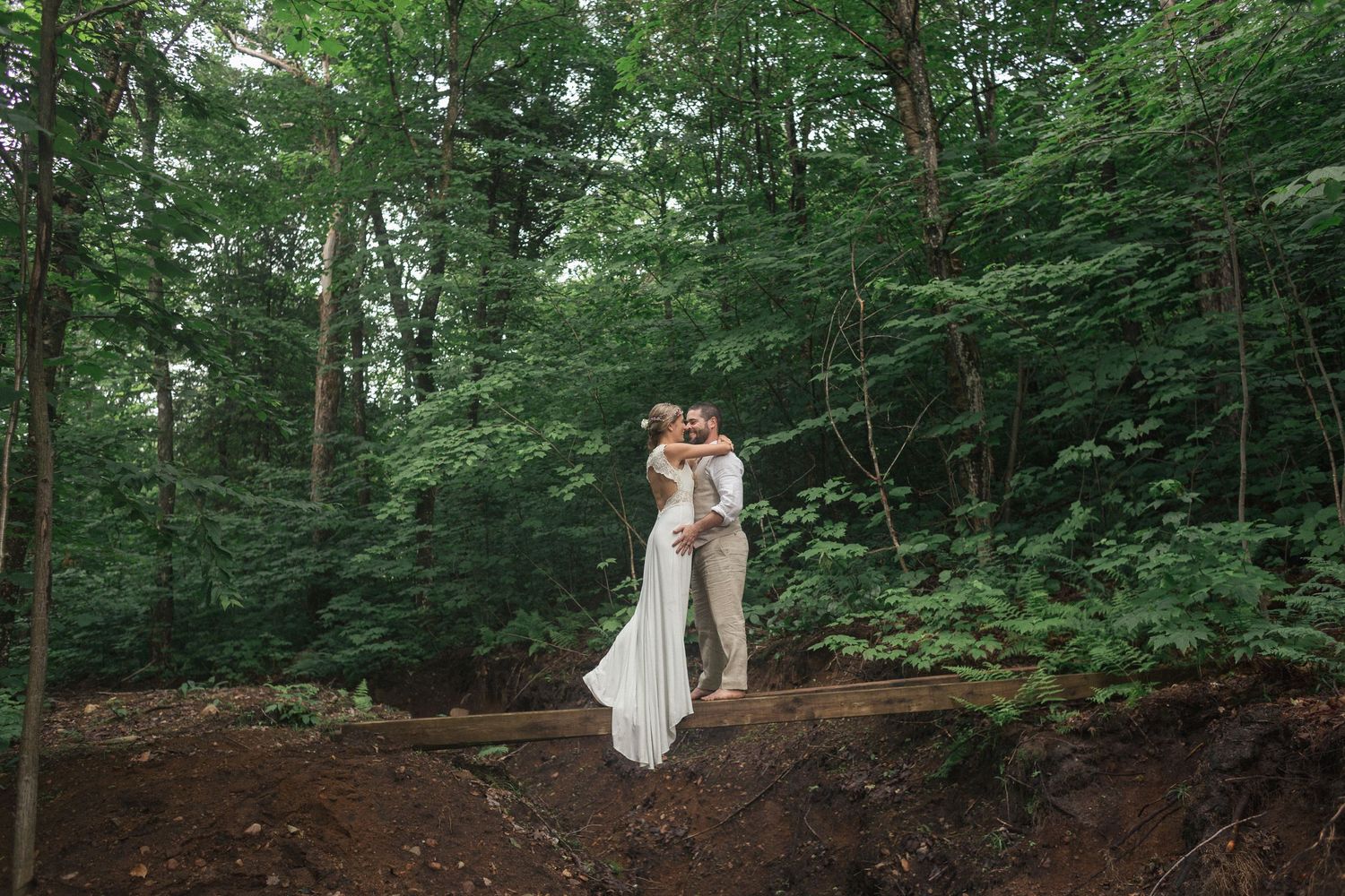 Un couple de mariés enlacés sur un tronc d'arbre en forêt.