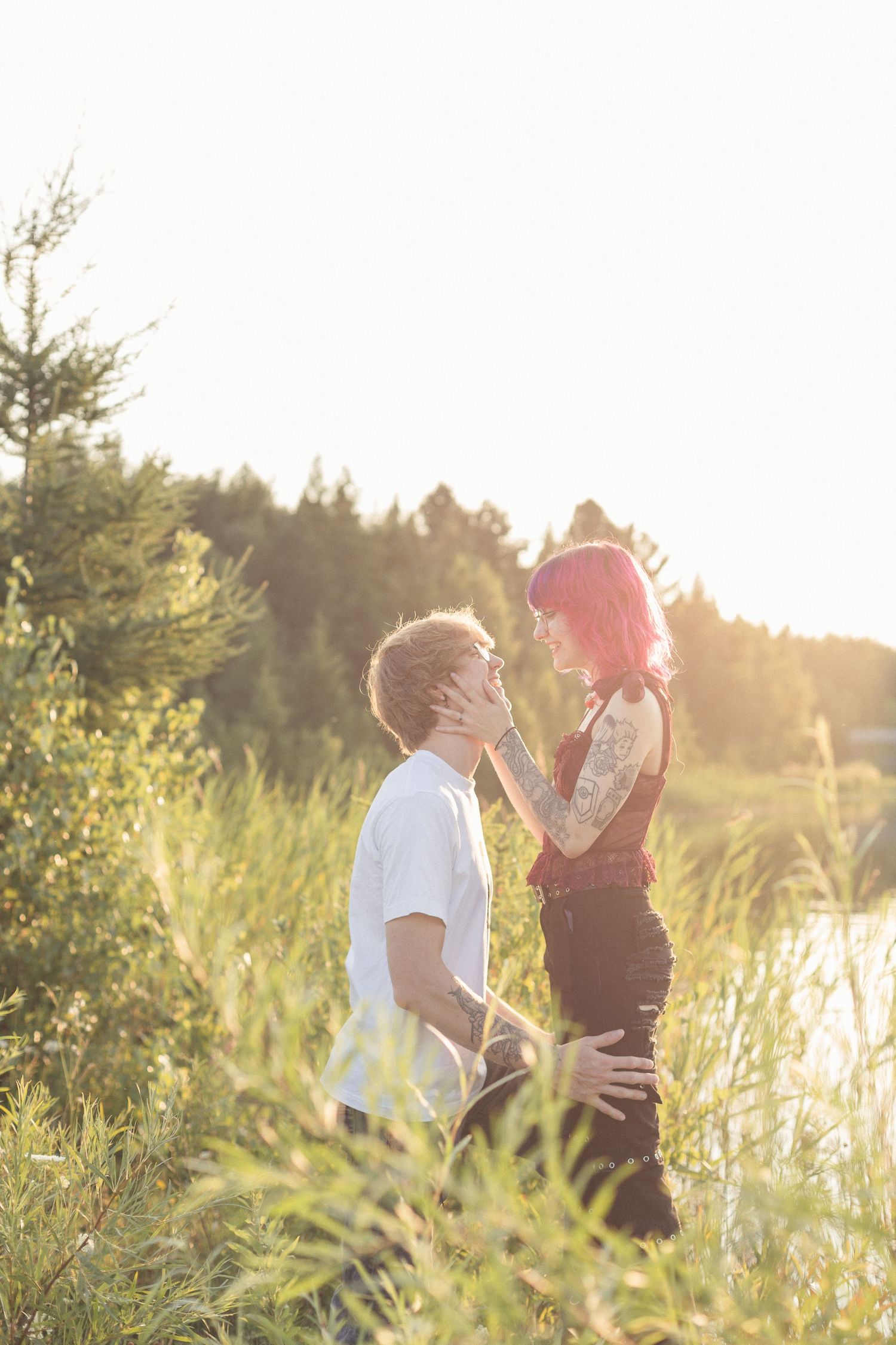 Une femme tenant le visage de son amoureux entre ses mains, le regardant avec un sourire  sous la lumière douce du coucher de soleil.