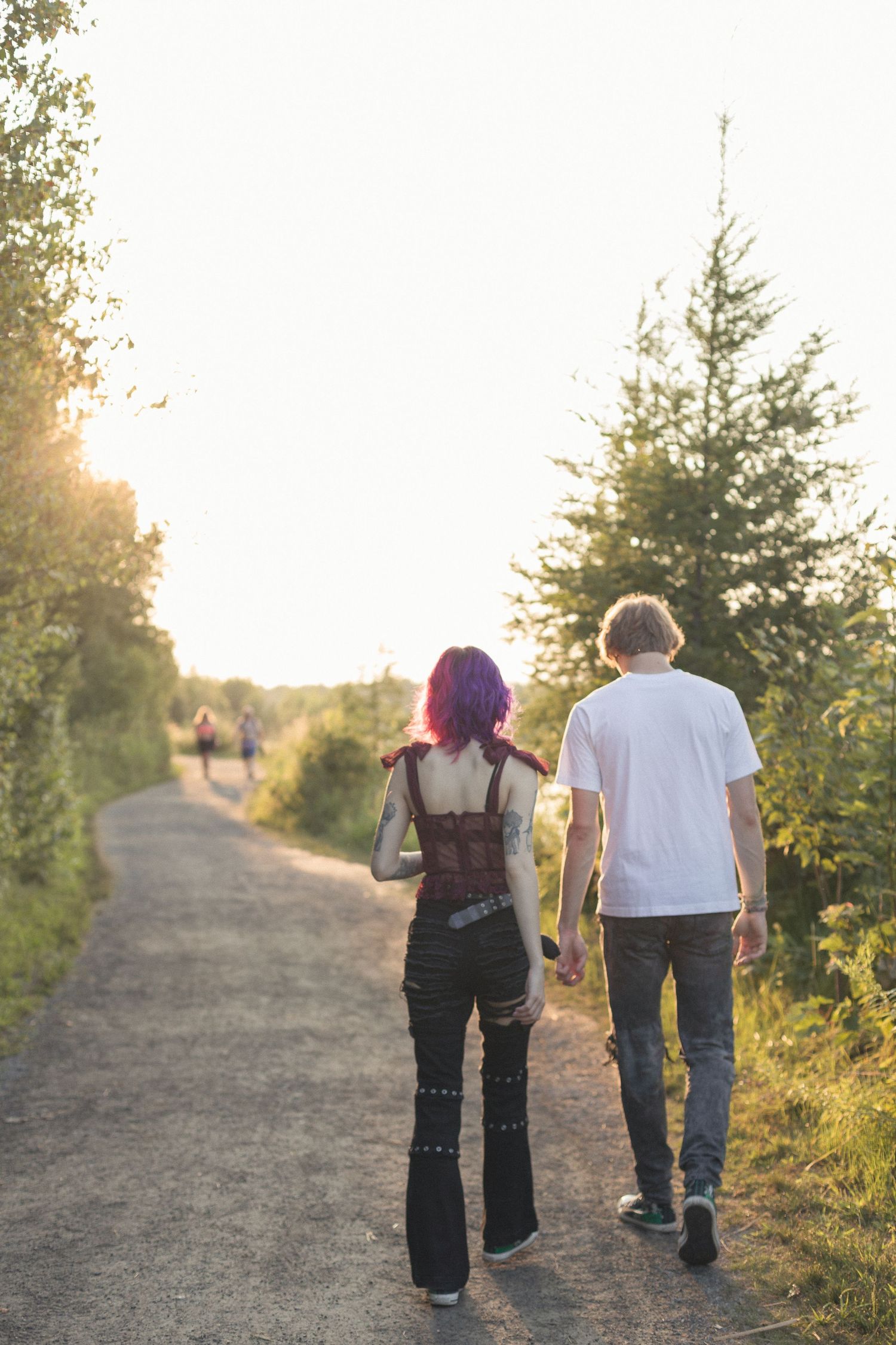Un couple de dos, marchant sur un chemin de terre, près d'un lac bordé par la forêt au coucher du soleil.