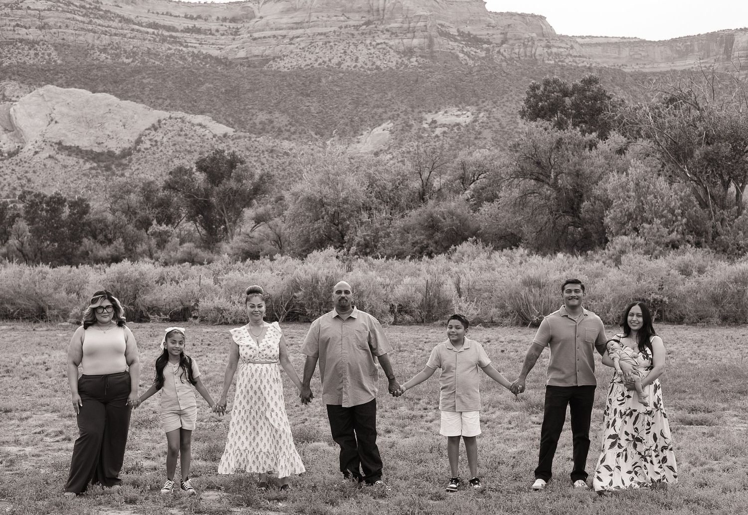 A group stands together in a field with scenic red rock canyon walls and desert vegetation in the background.