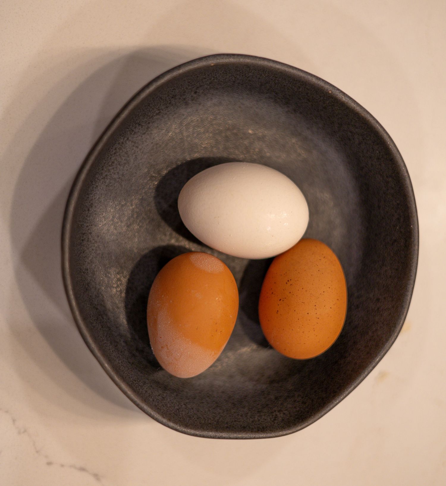 An egg is being cracked and poured into a white ceramic bowl showing the bright yellow yolk separating.