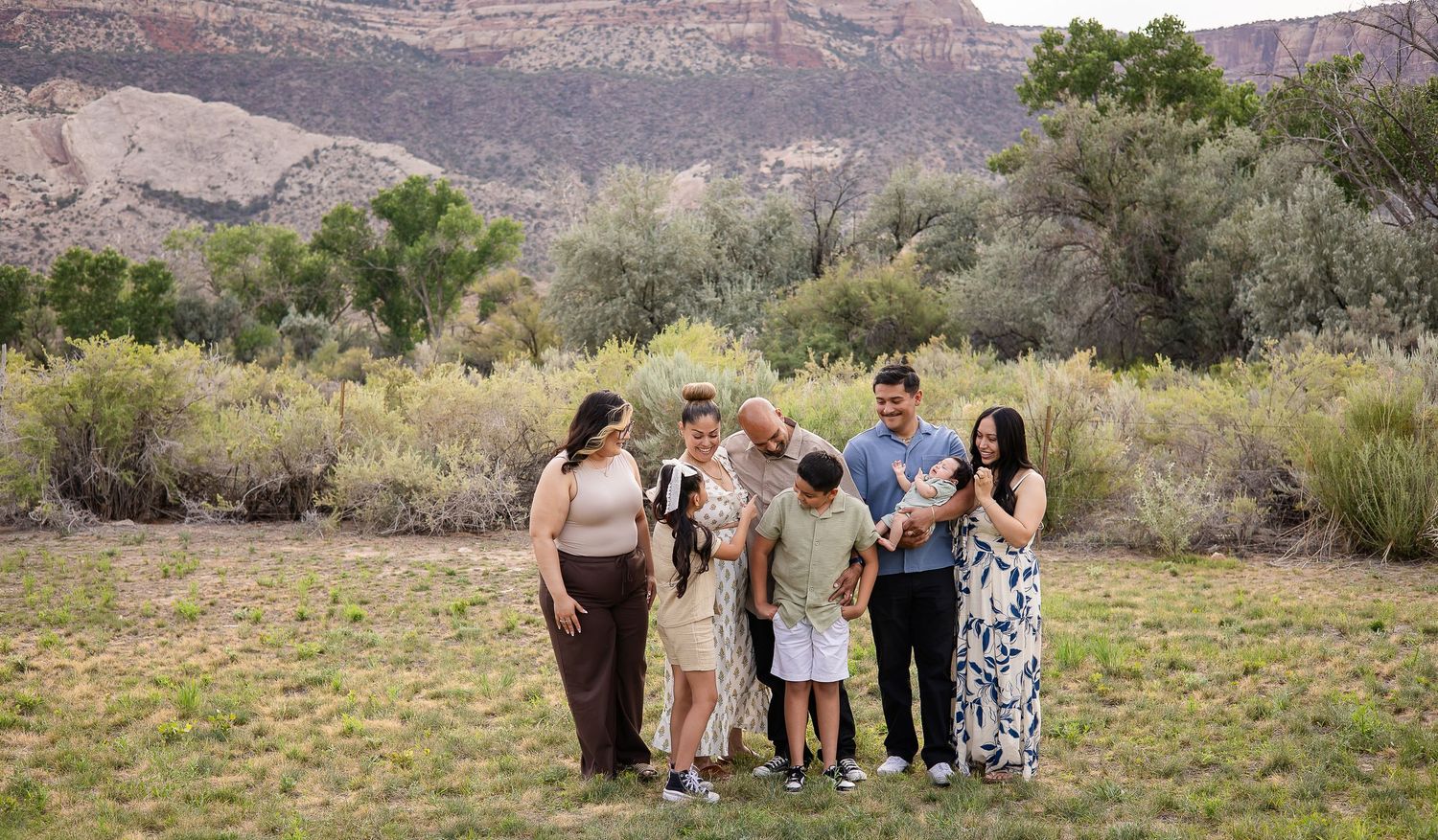 A group gathers on a scenic overlook with desert mountains and canyon landscapes in the background.