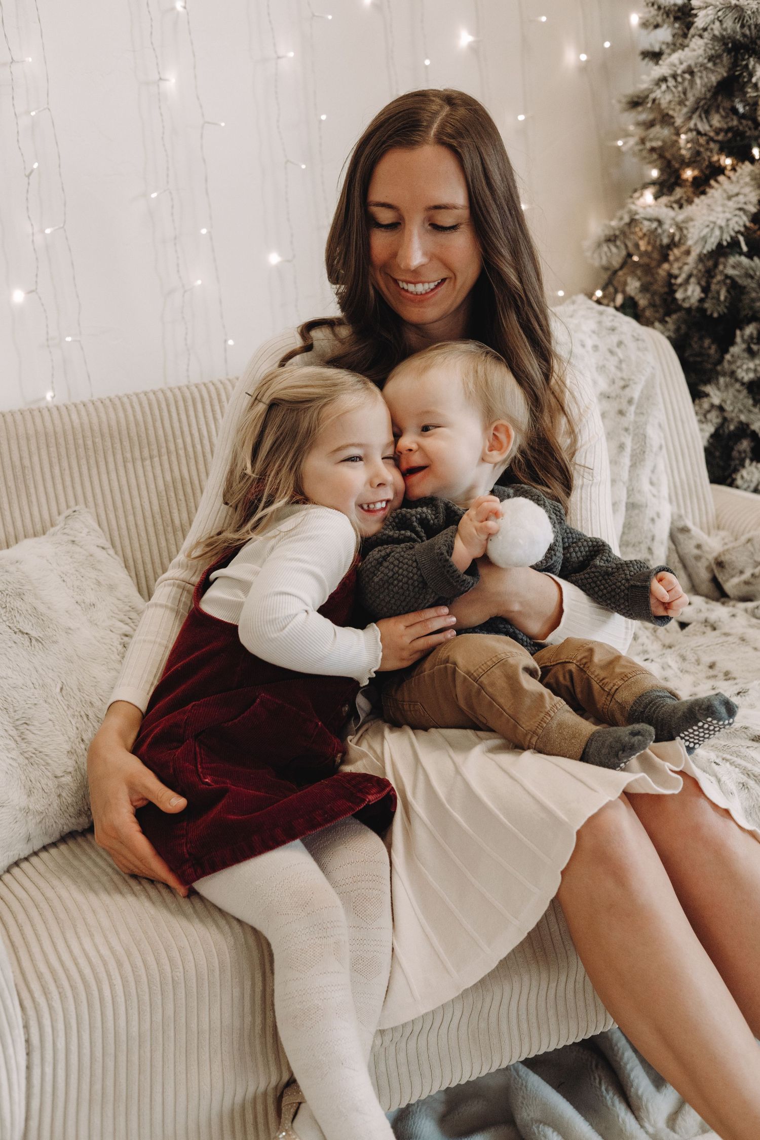 Cozy family moment on white couch with string lights and Christmas tree in background creates warm holiday atmosphere.
