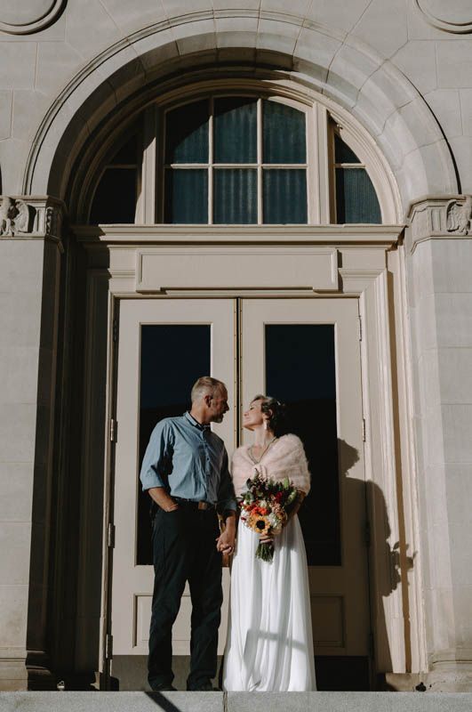 Newlyweds share an intimate moment under a grand architectural archway with beautiful natural lighting.