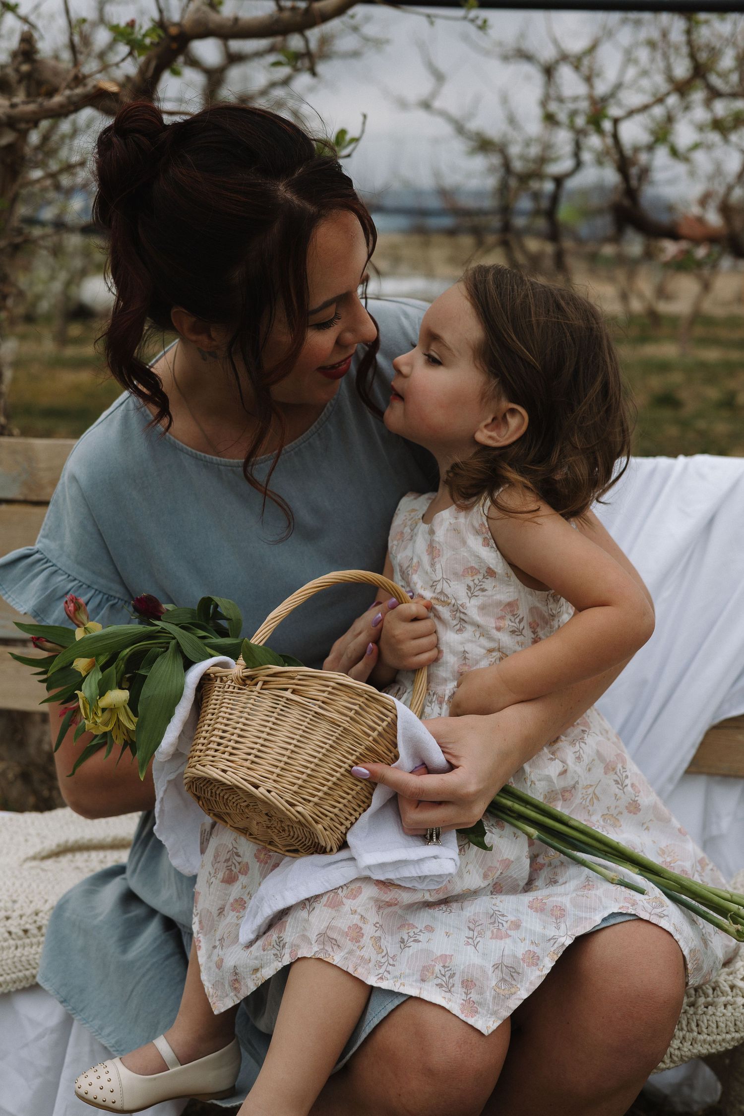 Sweet outdoor family moment on a blanket with a woven basket and greenery in soft natural light.