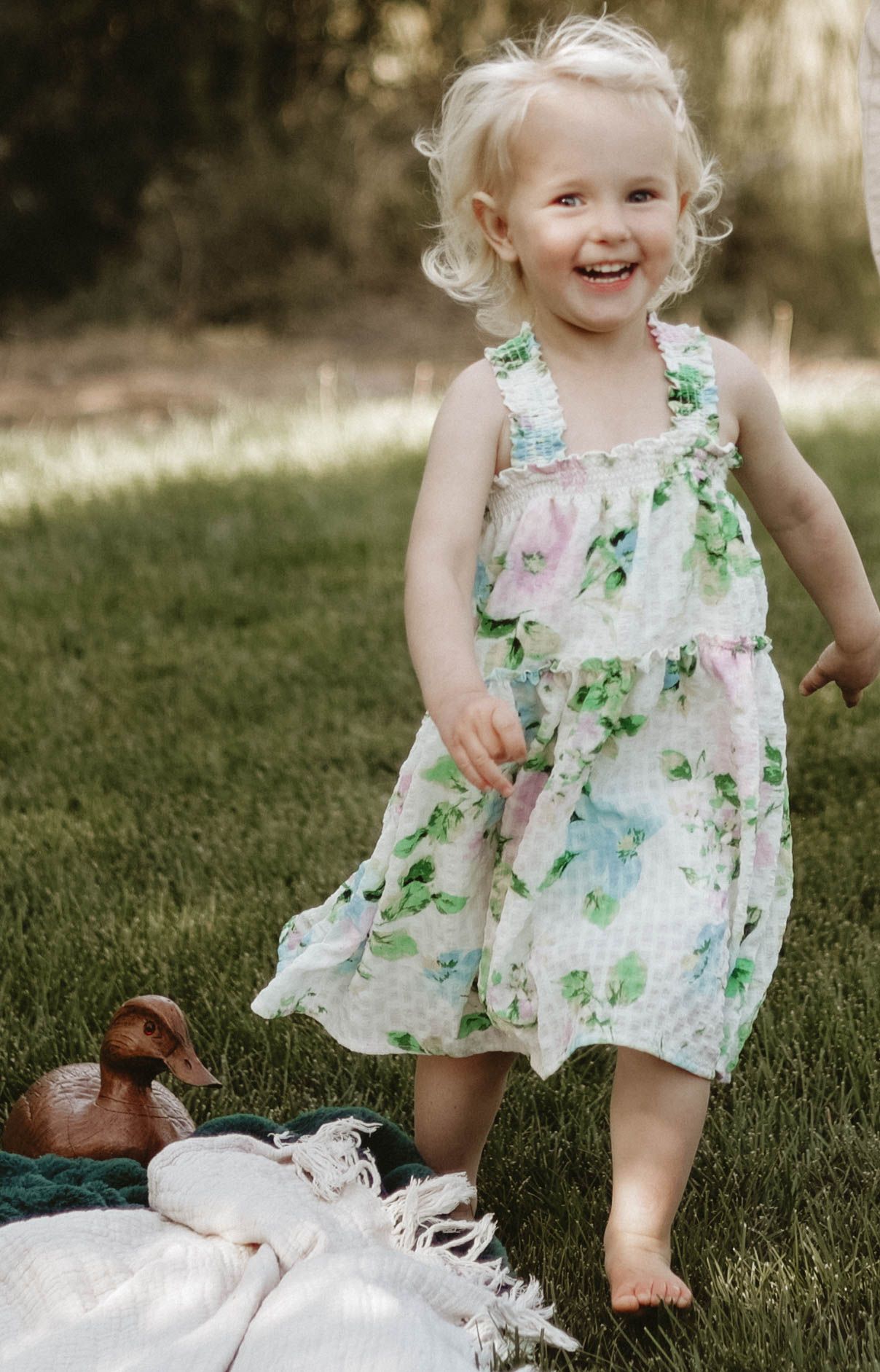 Toddler in floral dress playing and laughing on grass during outdoor photoshoot.