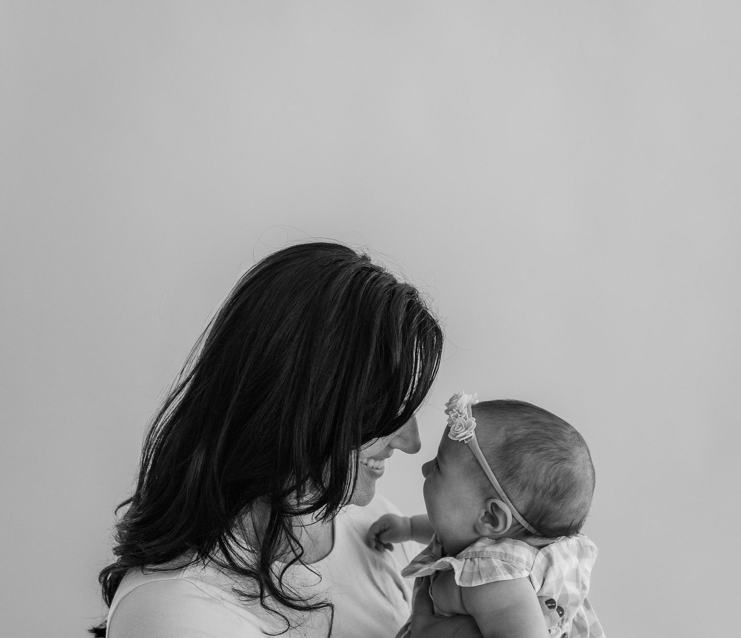 Black and white photo of a mother tenderly holding her newborn baby close, touching foreheads in an intimate moment.