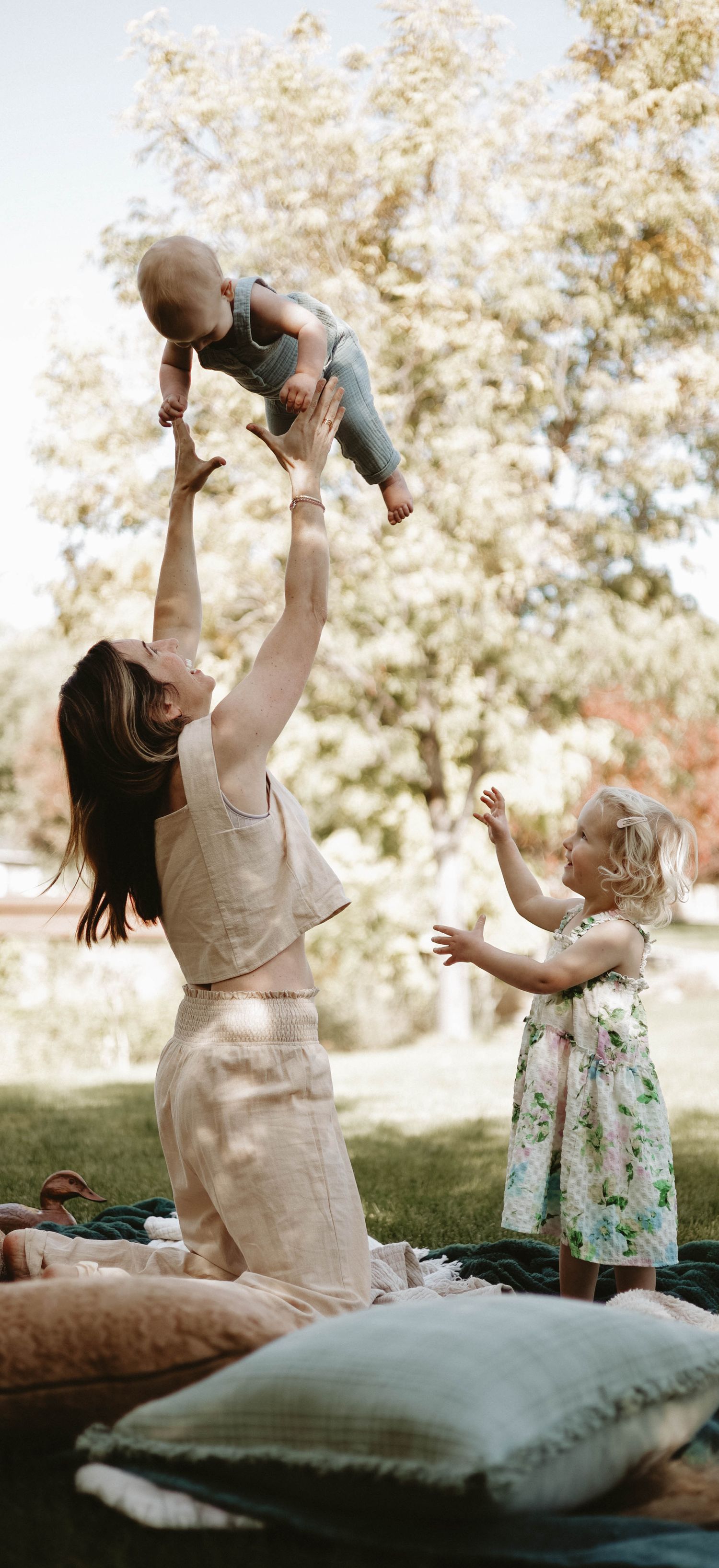 Playful outdoor family scene with everyone laughing and playing on cushions in a park setting.