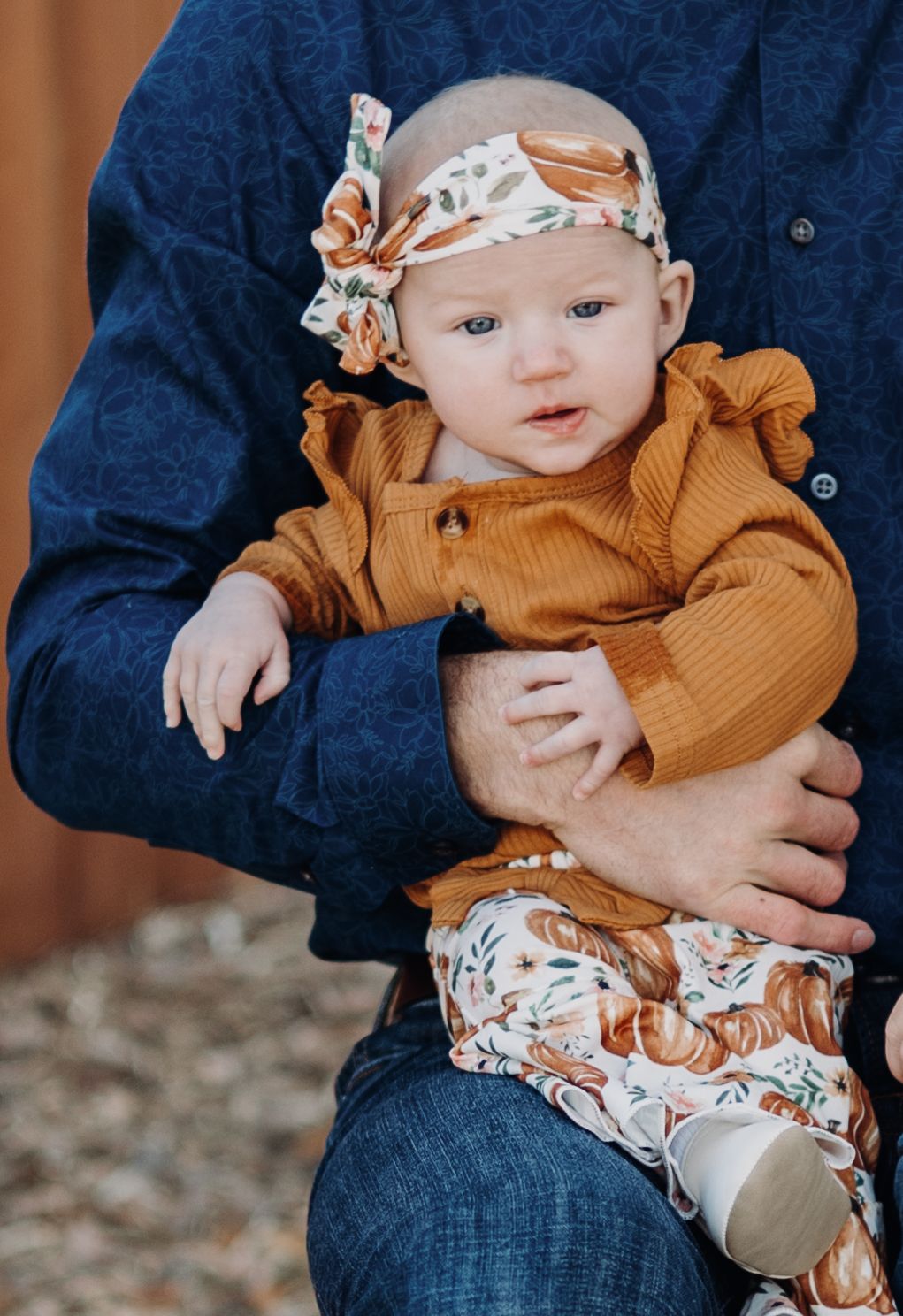 Baby wearing mustard-colored outfit and floral headband being held in blue denim lap in Grand Junction Colorado family session.