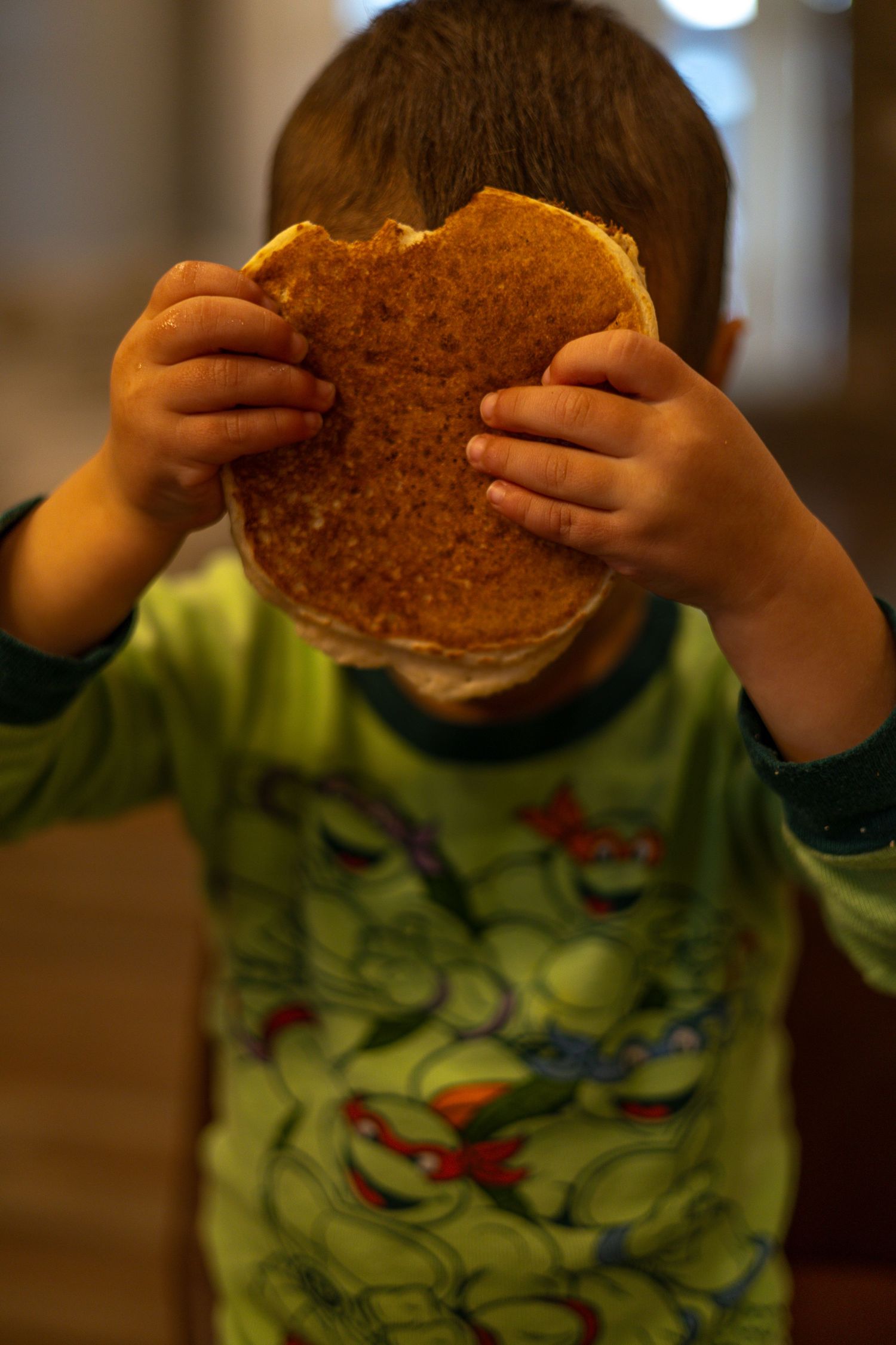 A sequence of photos showing hands holding a round sandwich against a dark background while wearing a green shirt.