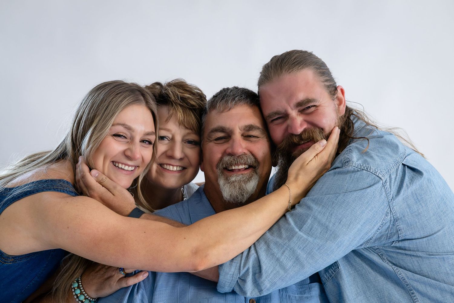 Four smiling family members in blue shirts hugging together for a warm portrait against a white background.