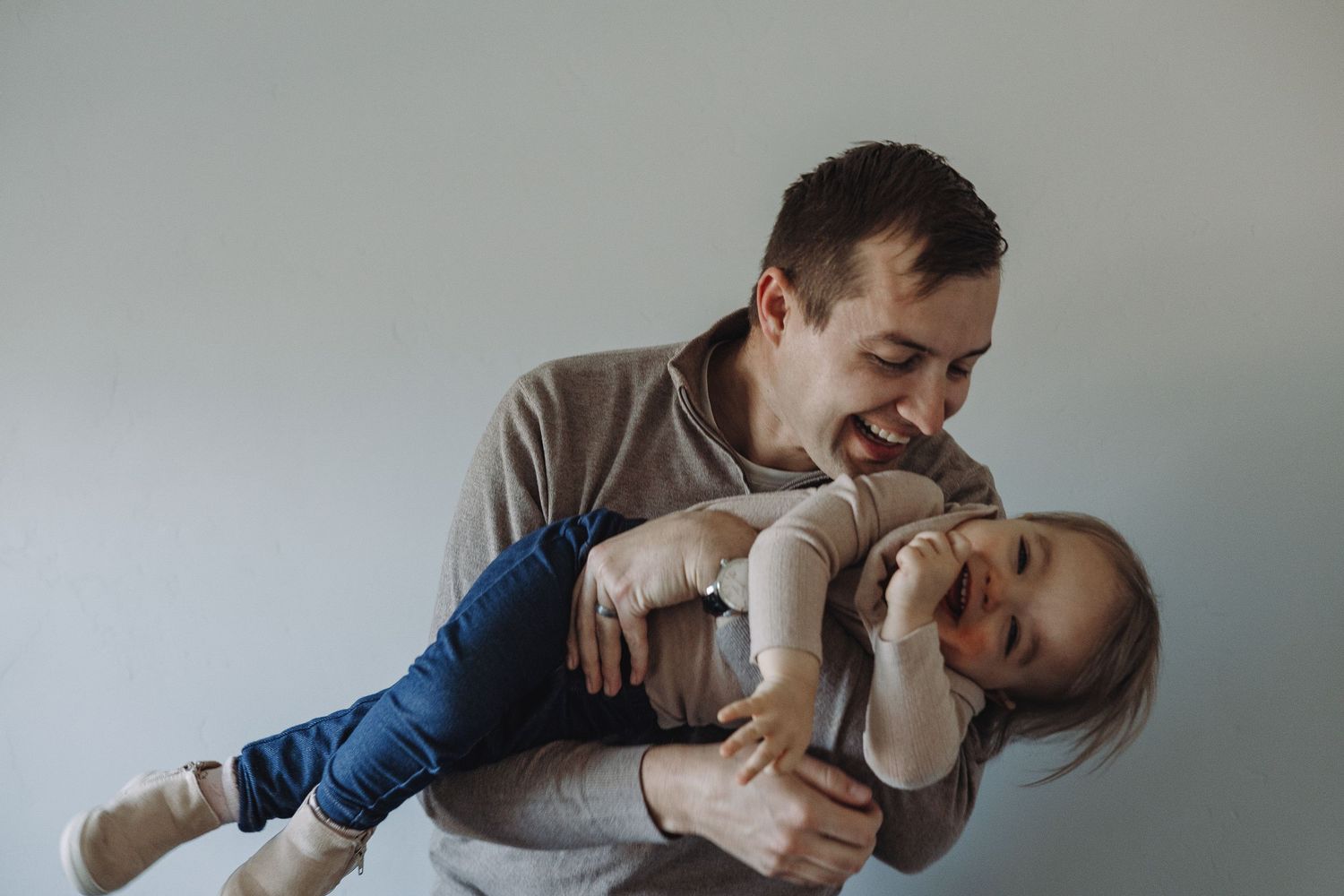 A loving moment of playful interaction as a parent and child laugh together on a gray background.