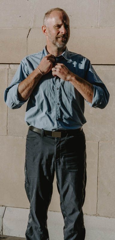 A person in business attire adjusts their shirt collar while standing against a light wall.