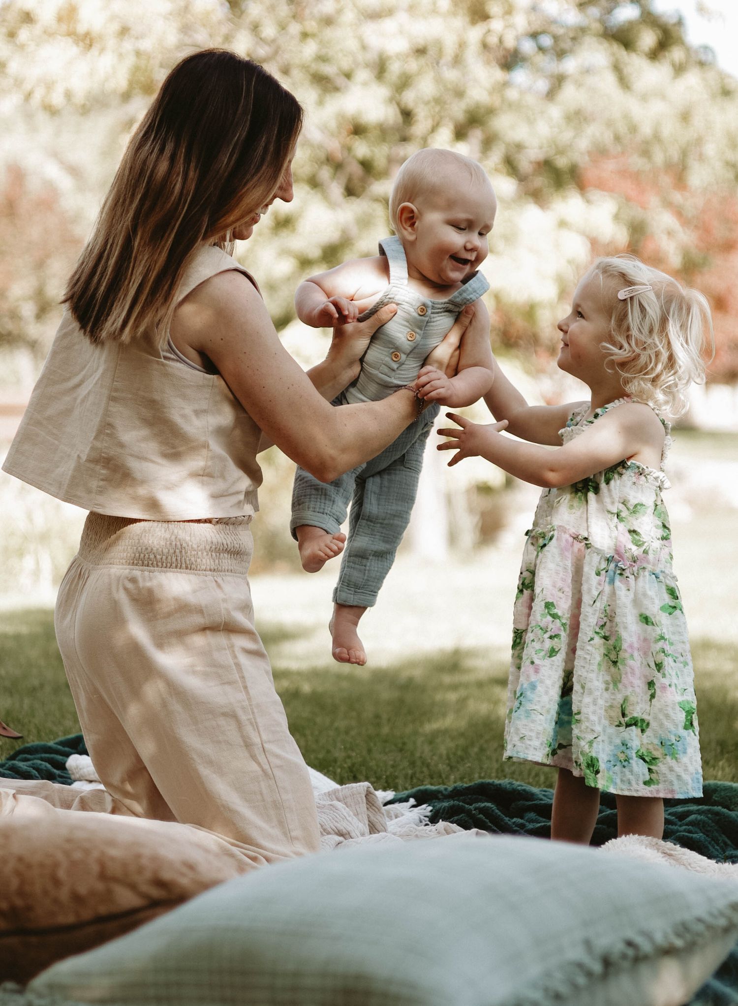 A joyful family moment outdoors on a blanket with cushions as they play and laugh together in natural sunlight.