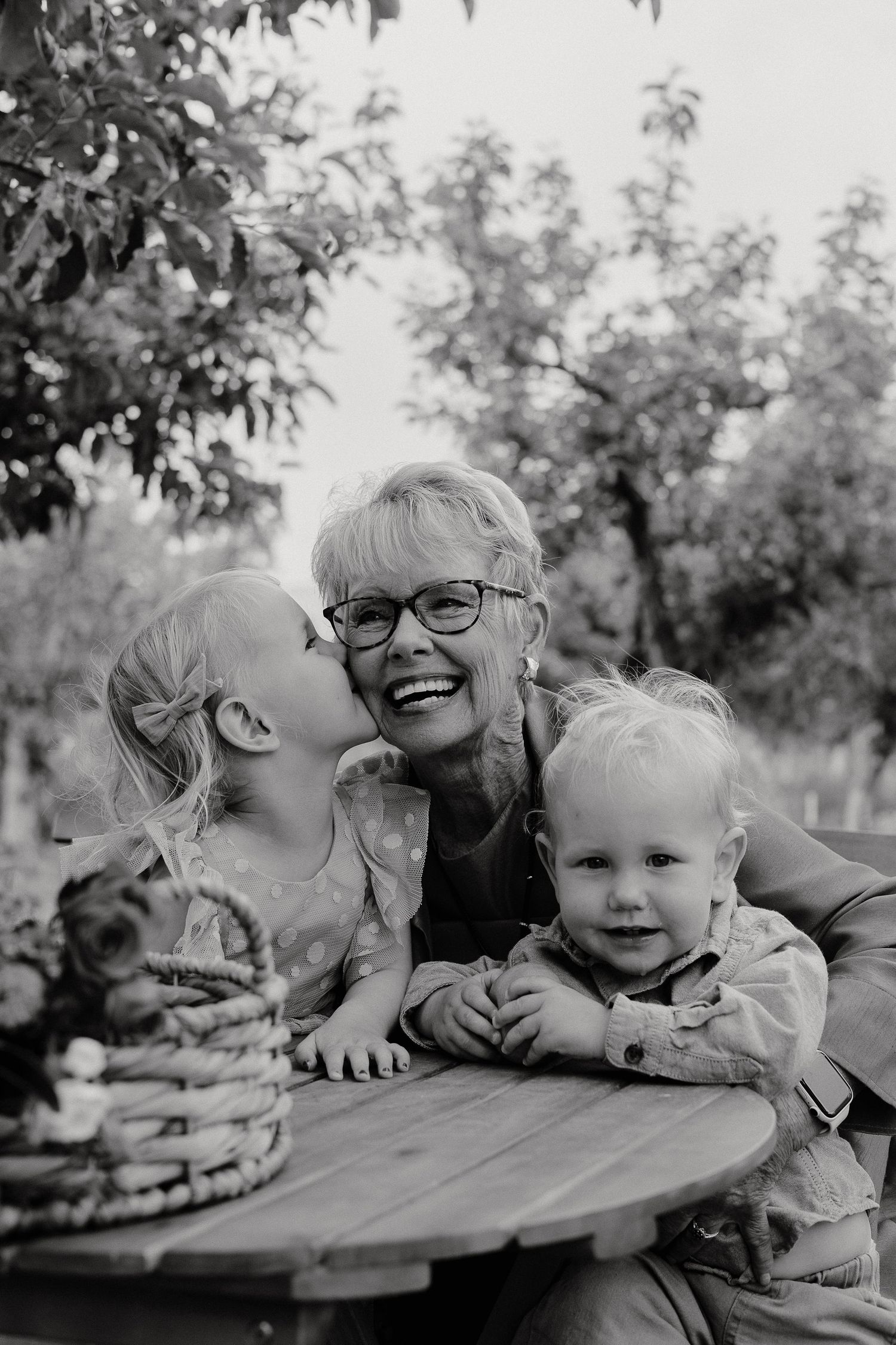 A black and white series of candid family moments outdoors showing playful interaction and laughter on a picnic table.