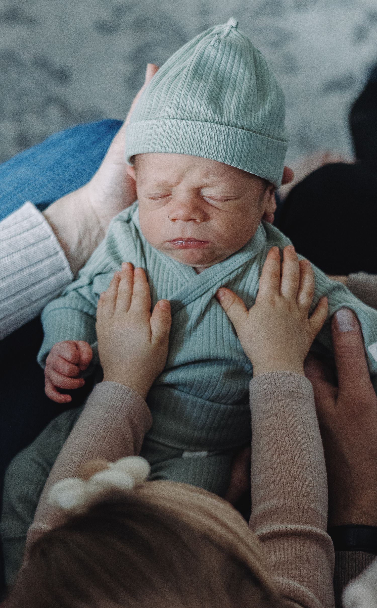 Series of gentle hands tenderly cradling a sleeping newborn baby wearing a soft mint green hat and outfit.
