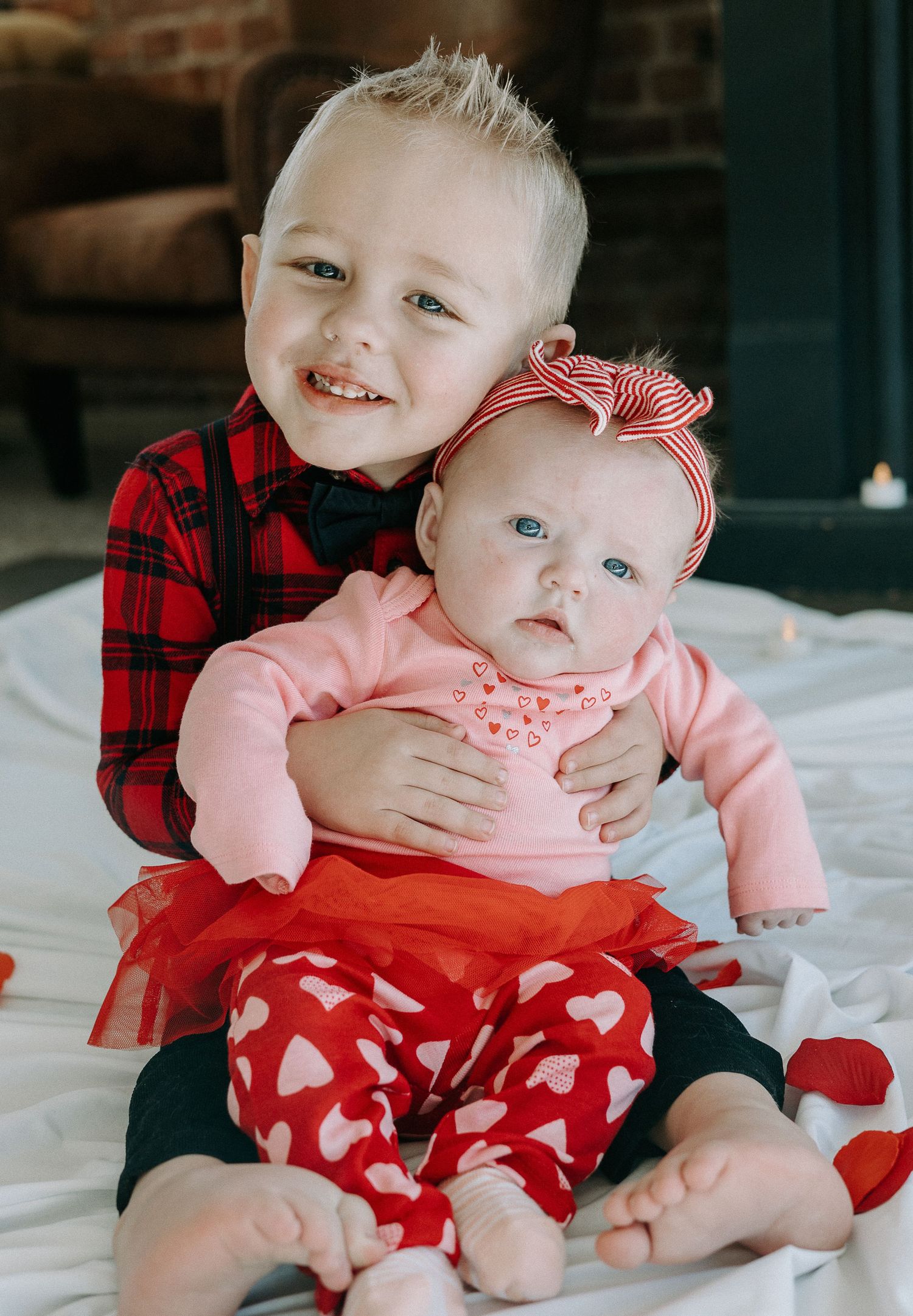 A heartwarming moment in front of an exposed brick wall as a figure in white lifts a baby wearing coral pink clothing.