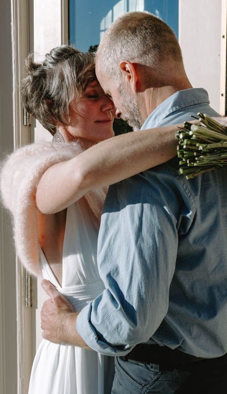 A romantic embrace between newlyweds in formal attire near a doorway.