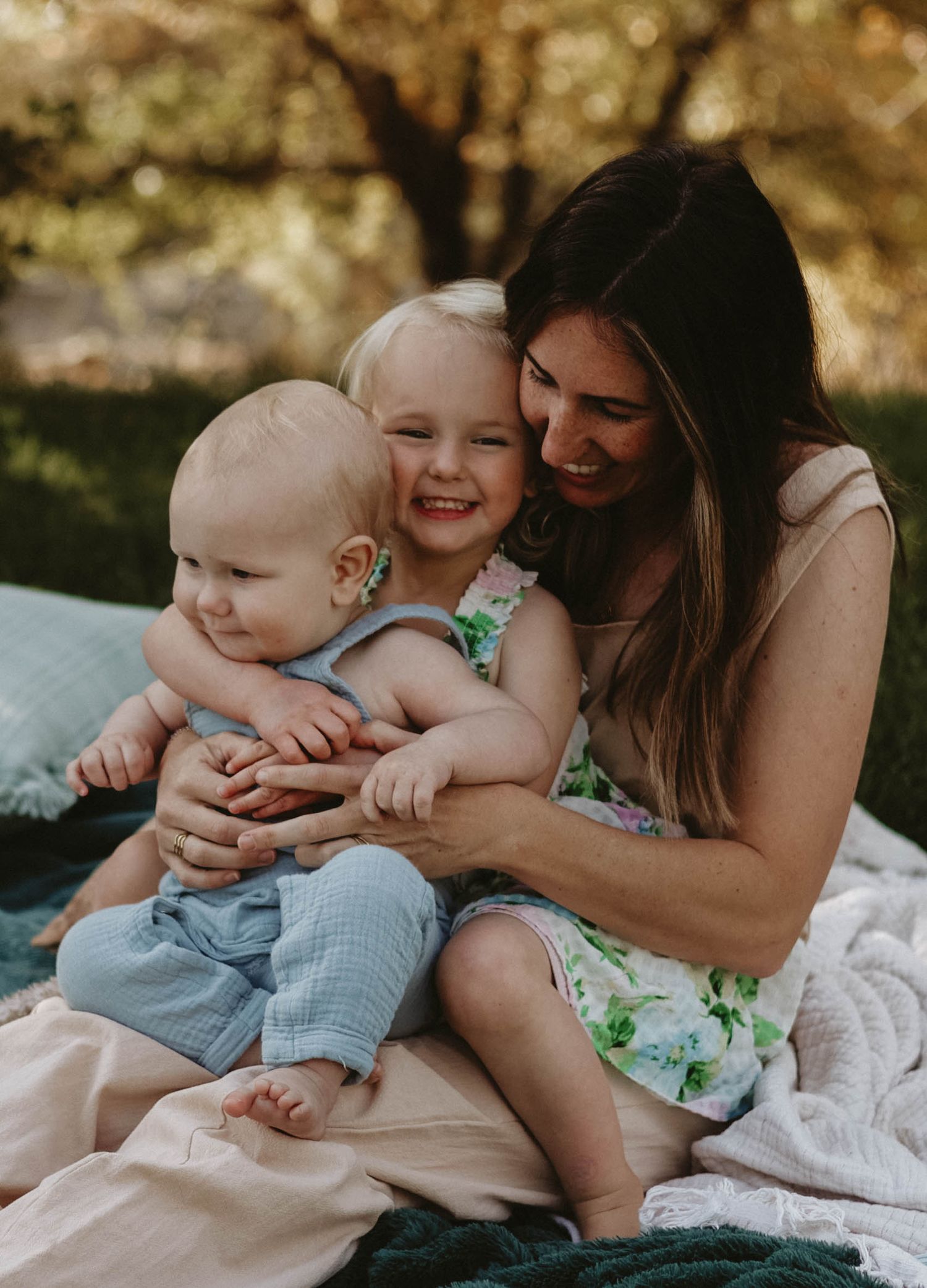 A tender family moment captured on a picnic blanket outdoors in warm sunlight.