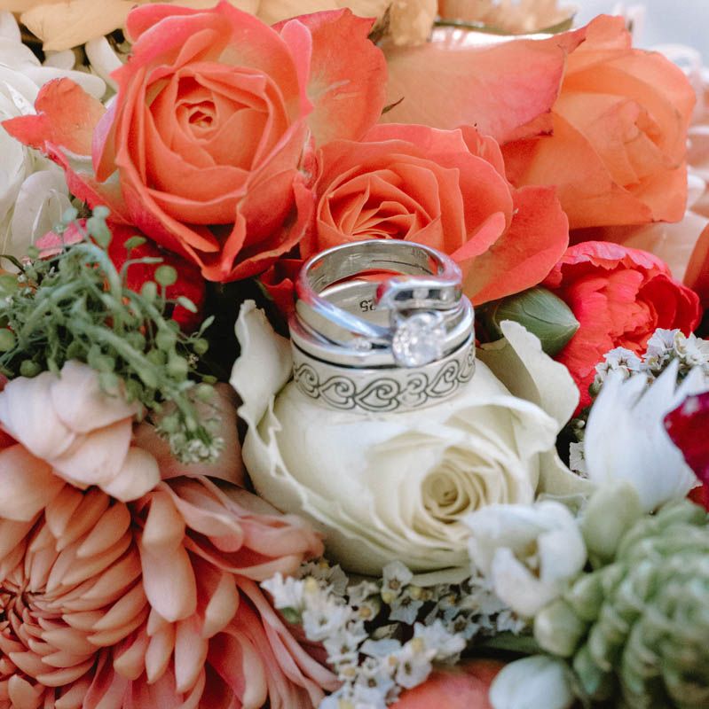 Close-up of coral and white roses with wedding rings resting on petals.