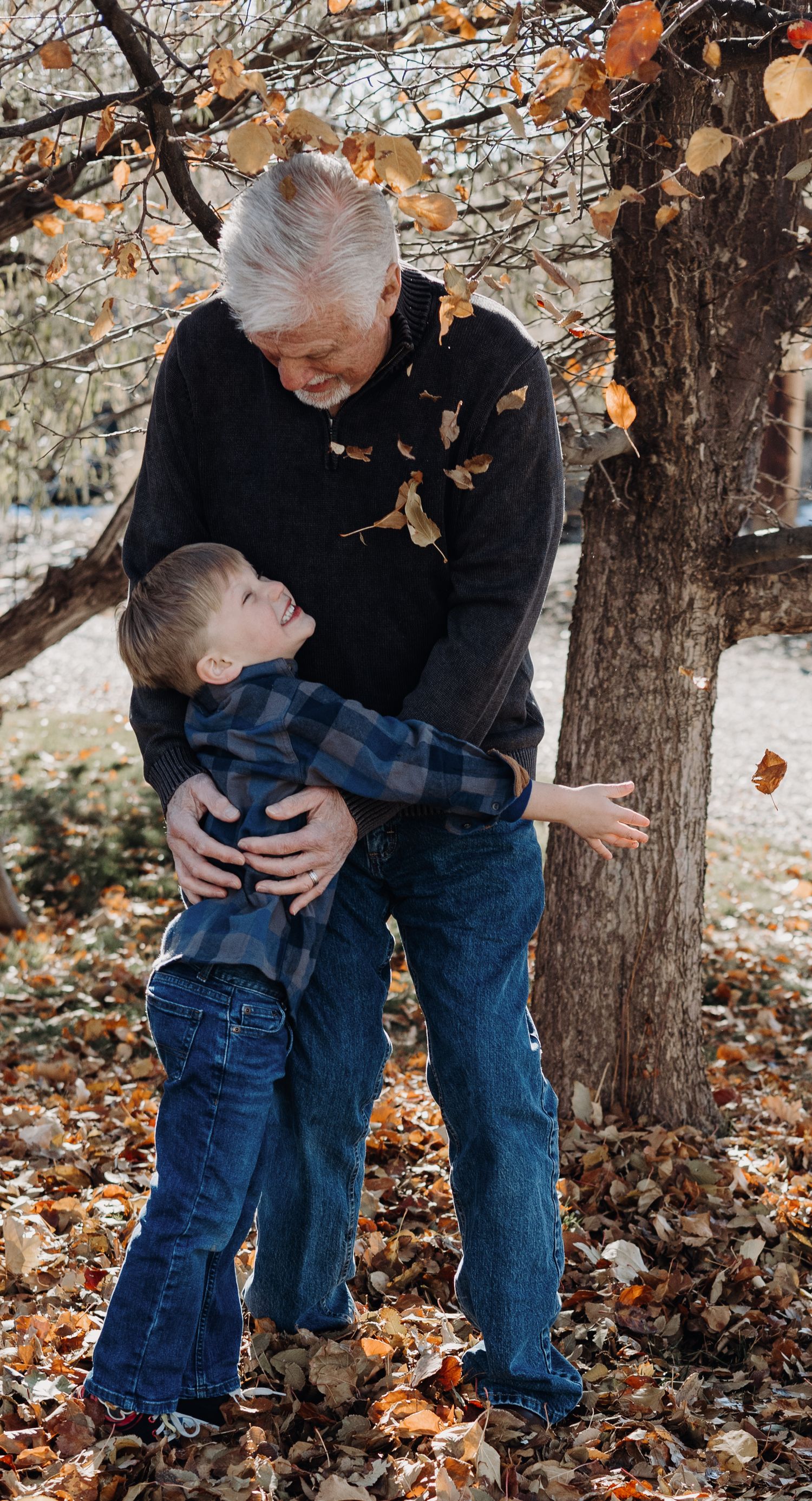 Candid moments between grandfather and grandson  among fallen autumn leaves near trees in Grand Junction Colorado.