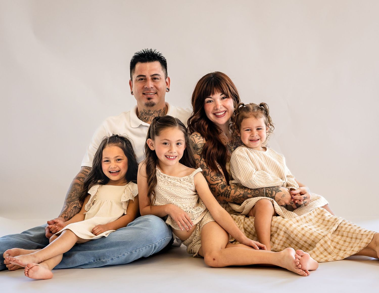Family of five posing together in a studio, parents with three young girls in coordinating neutral outfits.