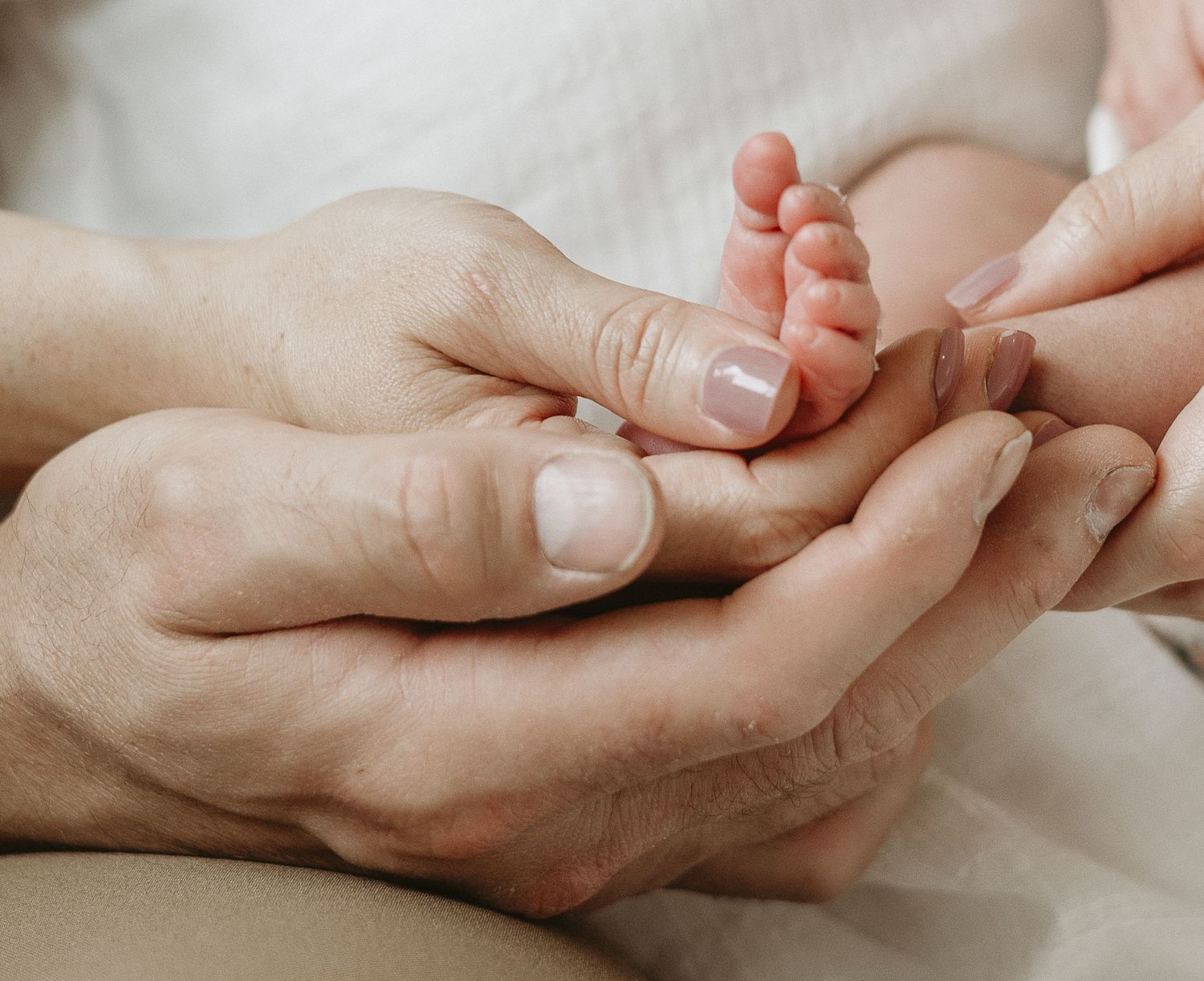 Adult hands gently hold tiny newborn baby feet wrapped in soft white fabric.