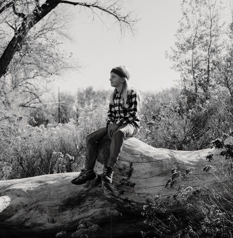Black and white artistic portrait of a young boy sitting on a fallen tree at Connected Lakes, Grand Junction, Colorado.