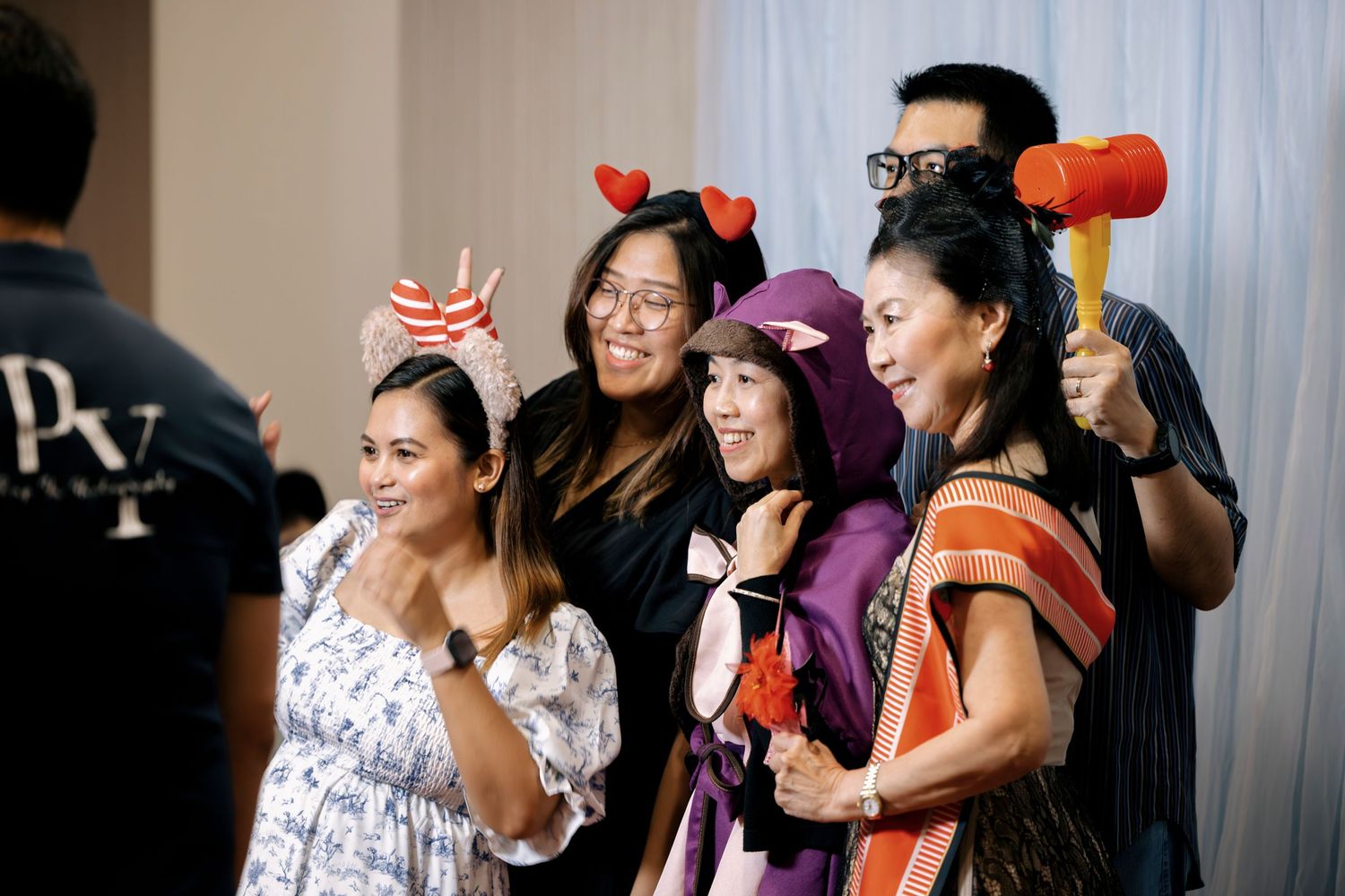Group of friends posing with fun props including devil horns and a mallet at a festive party event.