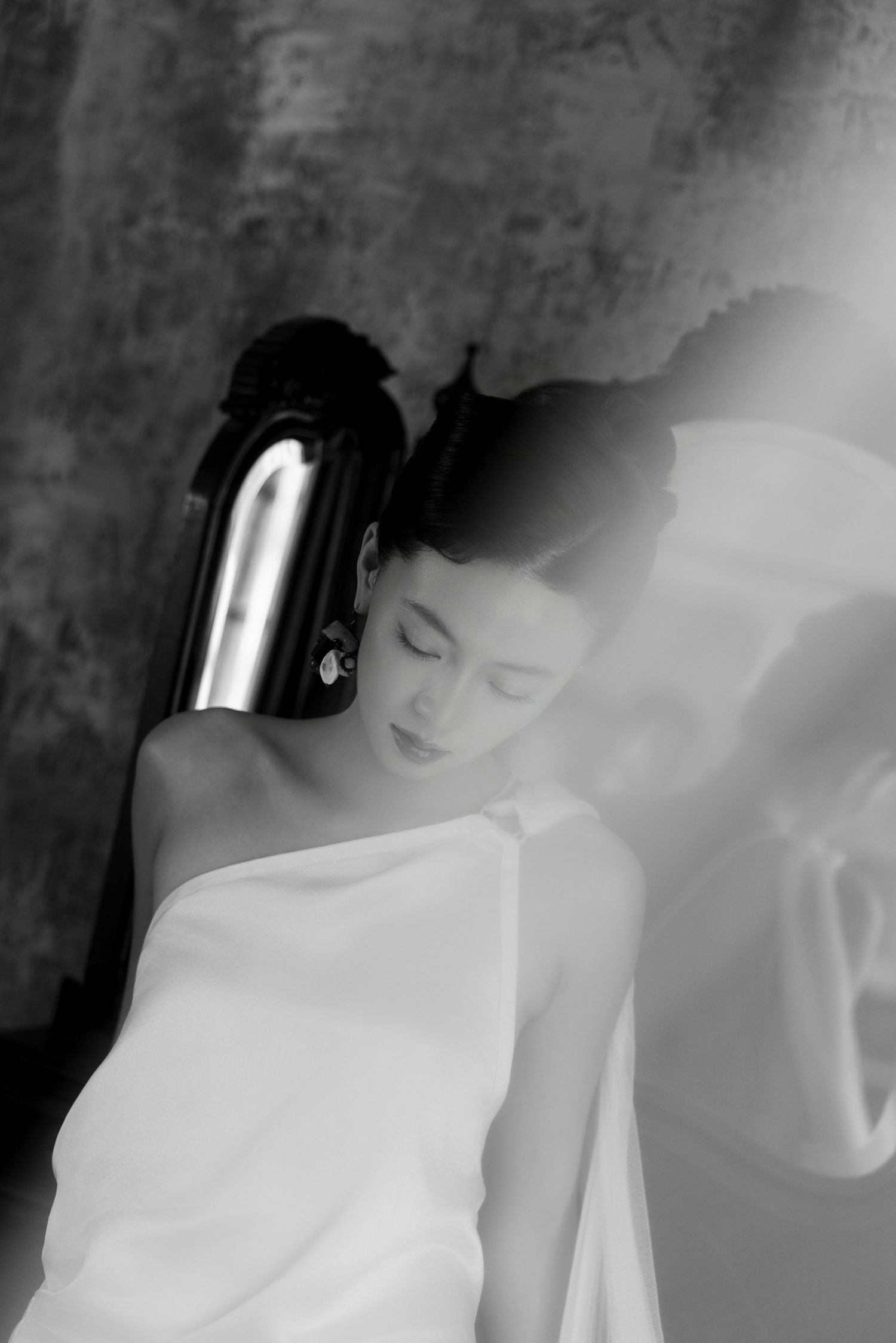 Black and white portrait of an elegant woman in white drape, eyes closed, with a sleek dark hair accessory.