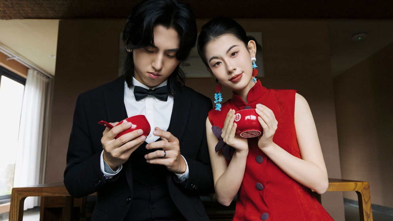 A stylish couple in formal attire examining red gift boxes, woman in red qipao and man in black tuxedo.