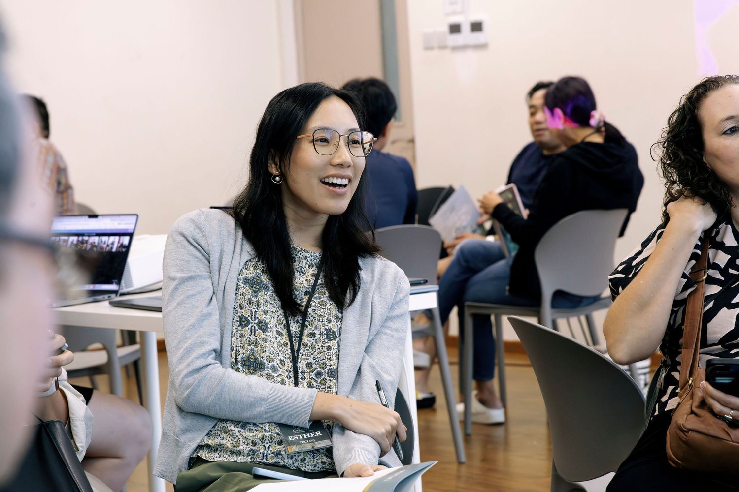 Smiling Asian woman with glasses engaged in discussion at a professional workshop or seminar.