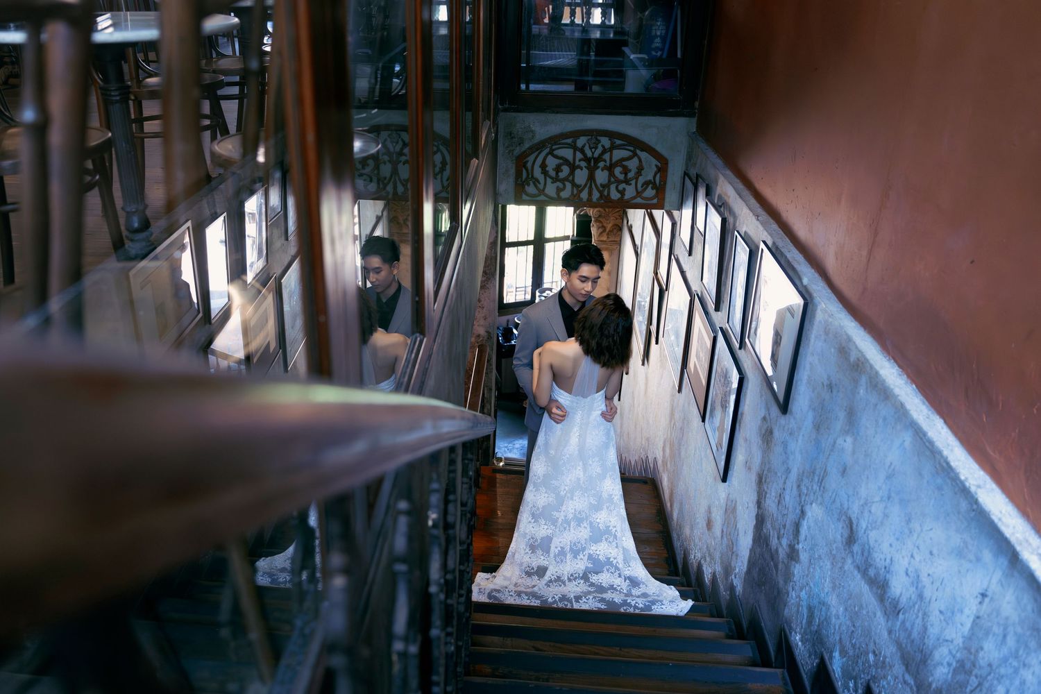 Groom helps bride with her lace wedding gown on a vintage staircase in a beautifully rustic interior.