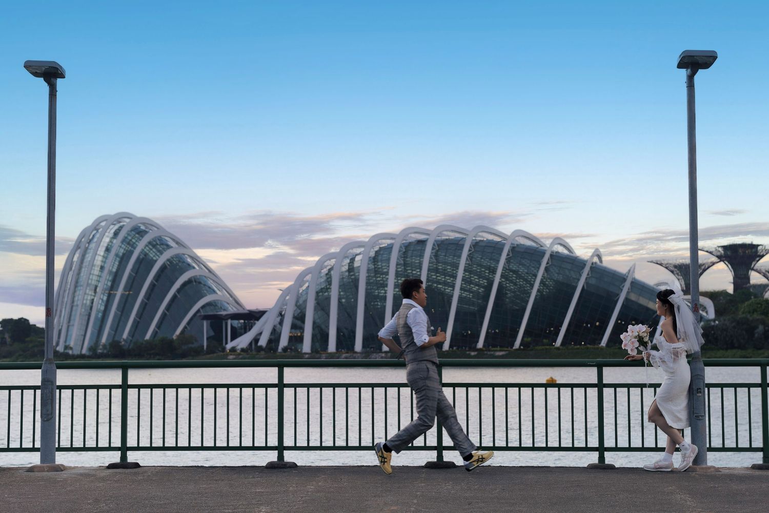 Couple jogging along a waterfront promenade at dusk with Gardens by the Bay domes in Singapore.